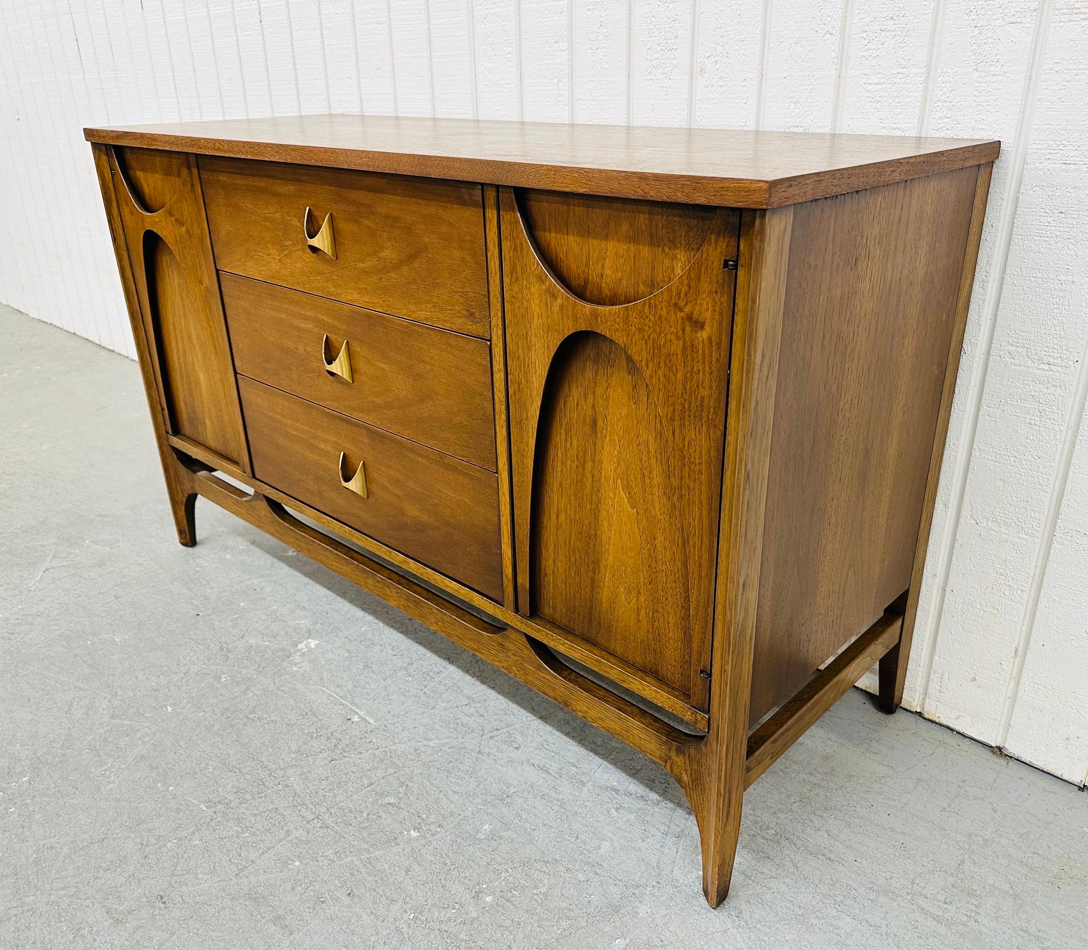 This listing is for an iconic Mid-Century Modern Broyhill Brasilia Walnut Server. Featuring a straight line design, two doors with the sculpted Brasilia pulls, the doors open up to fixed shelving storage space, three drawers in the center with