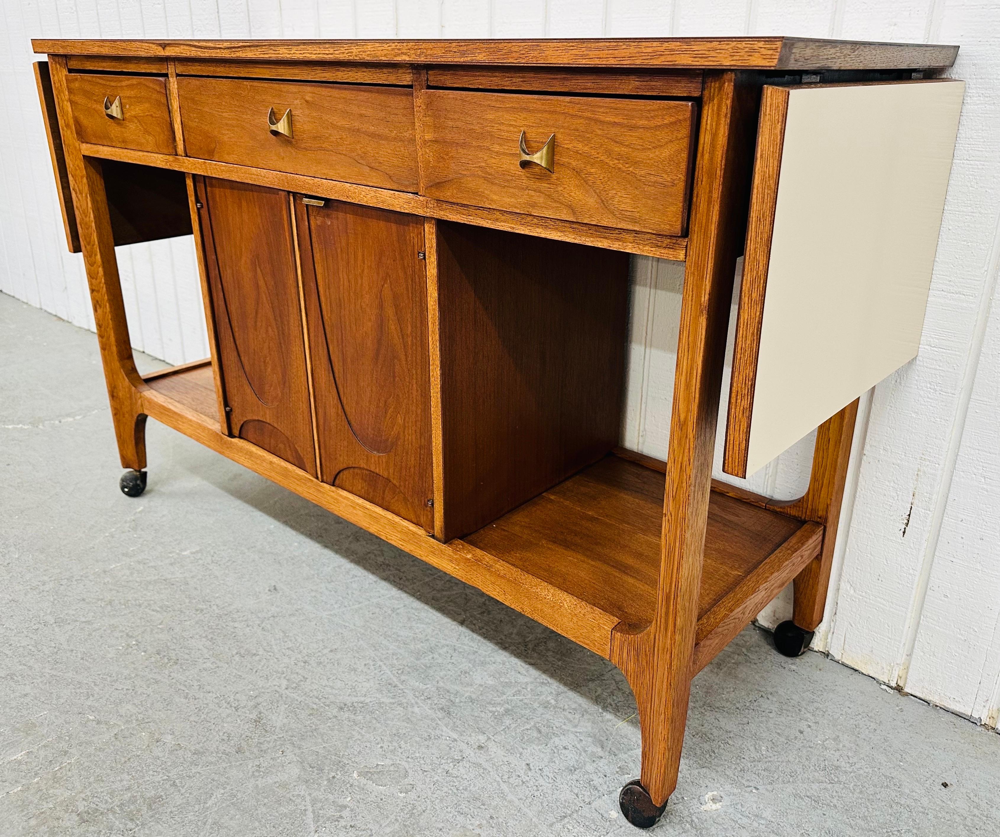 This listing is for a Mid-Century Modern Broyhill Brasilia Walnut Serving Cart. Featuring a straight line design, rectangular laminated top with drop sides that extend the serving area to 70” L, three drawers with the iconic Brasilia brass hardware,