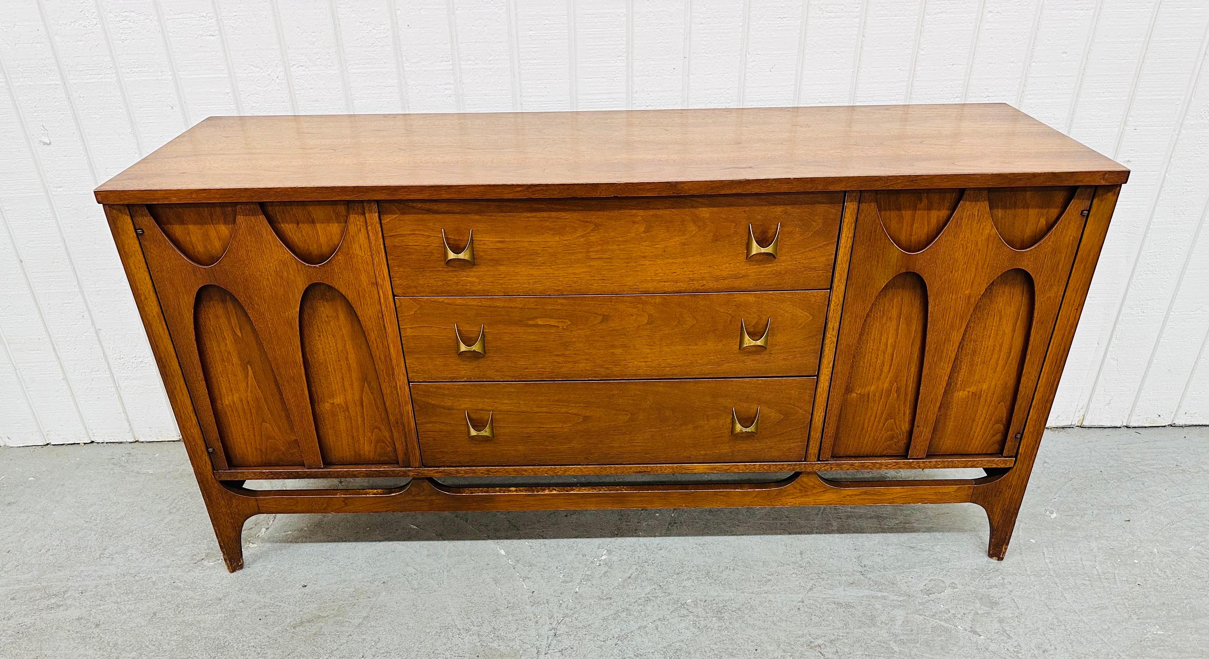 This listing is for a Mid-Century Modern Broyhill Brasilia Walnut Sideboard. Featuring a straight line design, two doors with the iconic sculpted Brasilia pulls, storage space, three drawers in the center, the original Brasilia hardware, and a