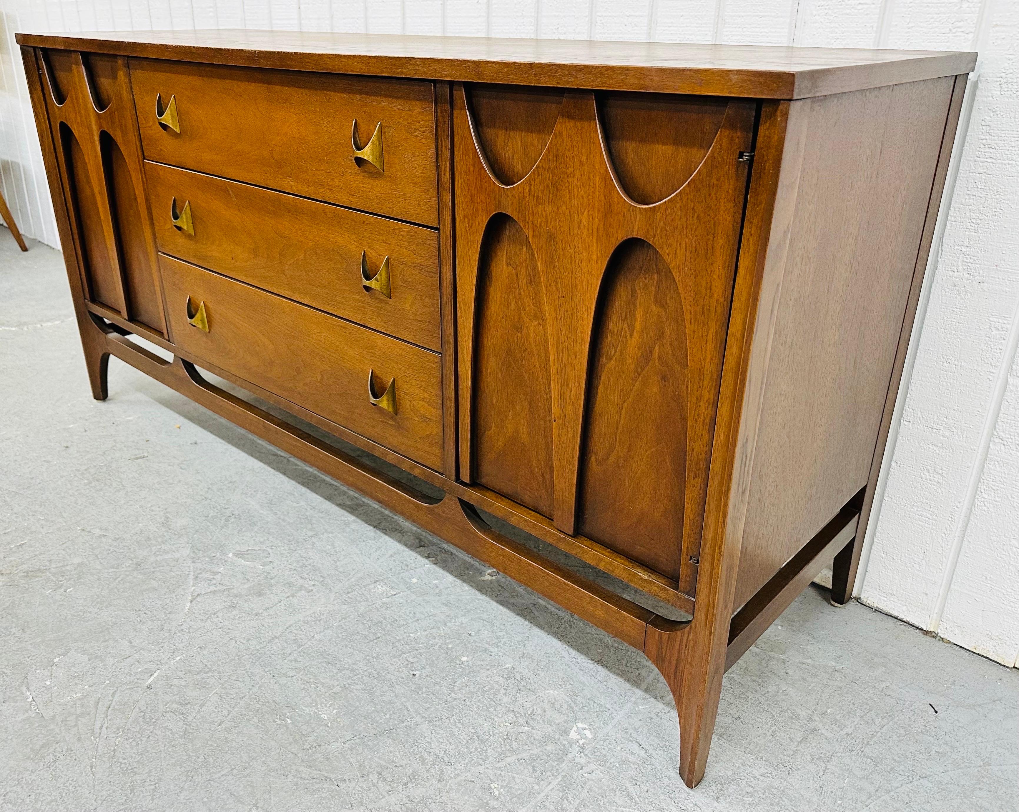 This listing is for a Mid-Century Modern Broyhill Brasilia Walnut Sideboard. Featuring a straight line design, sculpted doors on each side that open up to storage space, three drawers in the center, original brass Brasilia pulls, modern legs with