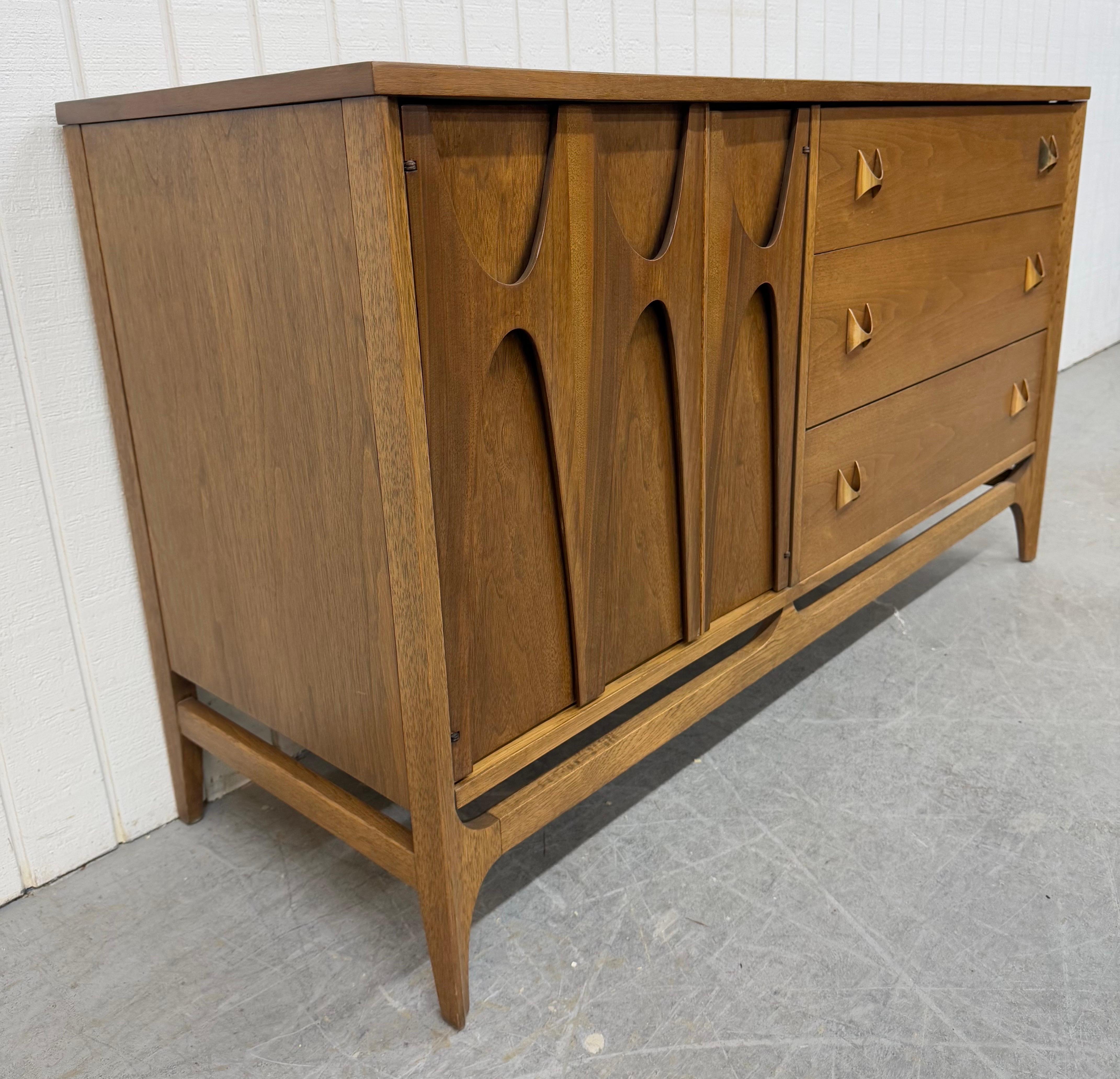 This listing is for a Mid-Century Modern Broyhill Brasilia Walnut Sideboard. Featuring a straight line design, sculpted doors that open up to storage space, three drawers with original brass hardware, modern legs with stretcher base, and a
