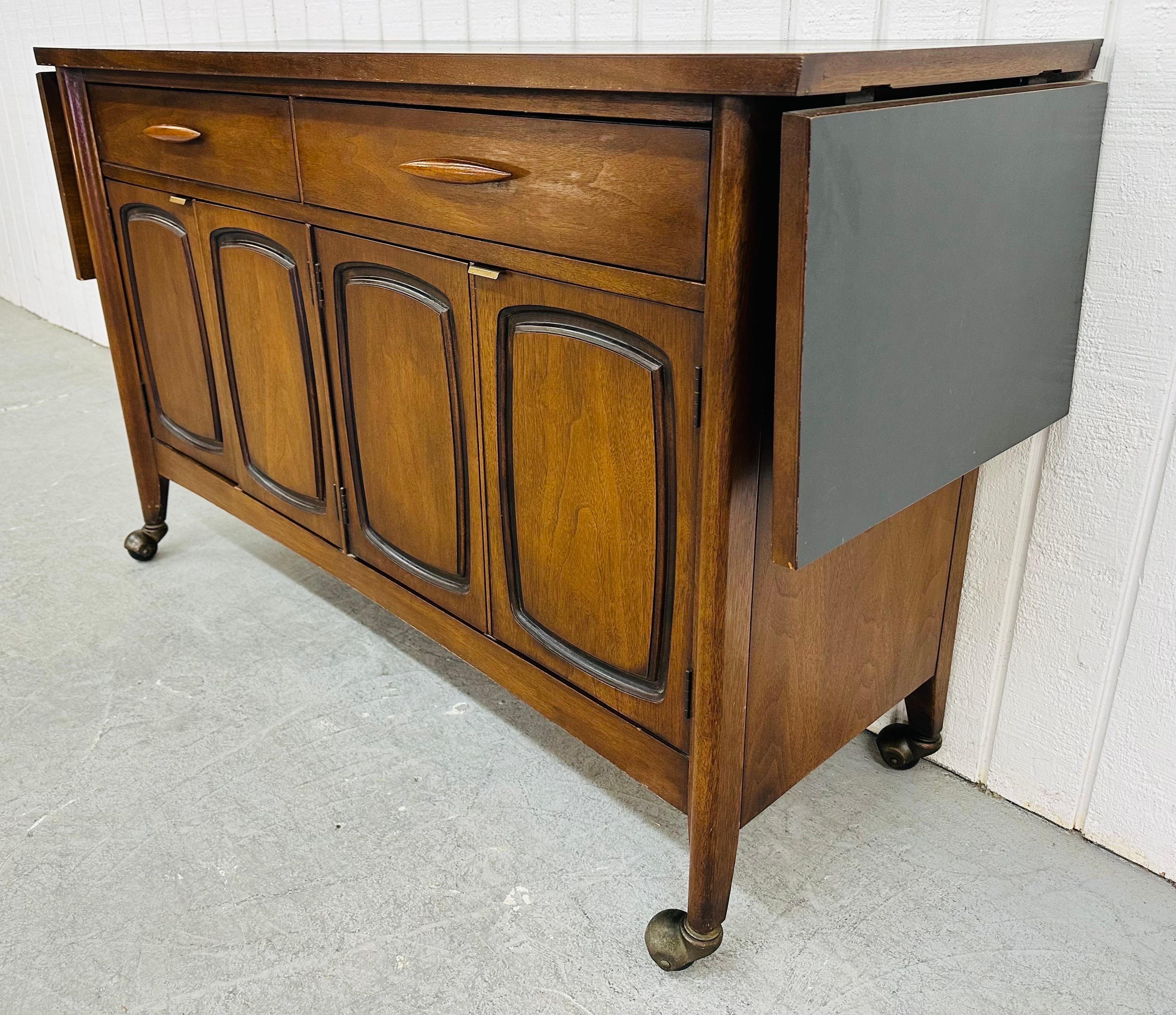 This listing is for a Mid-Century Modern Broyhill Emphasis Walnut Bar Cart. Featuring a straight line design, rectangular laminated serving top that expands up to 70” L, two drawers with sculpted wooden pulls, four door that open up to storage