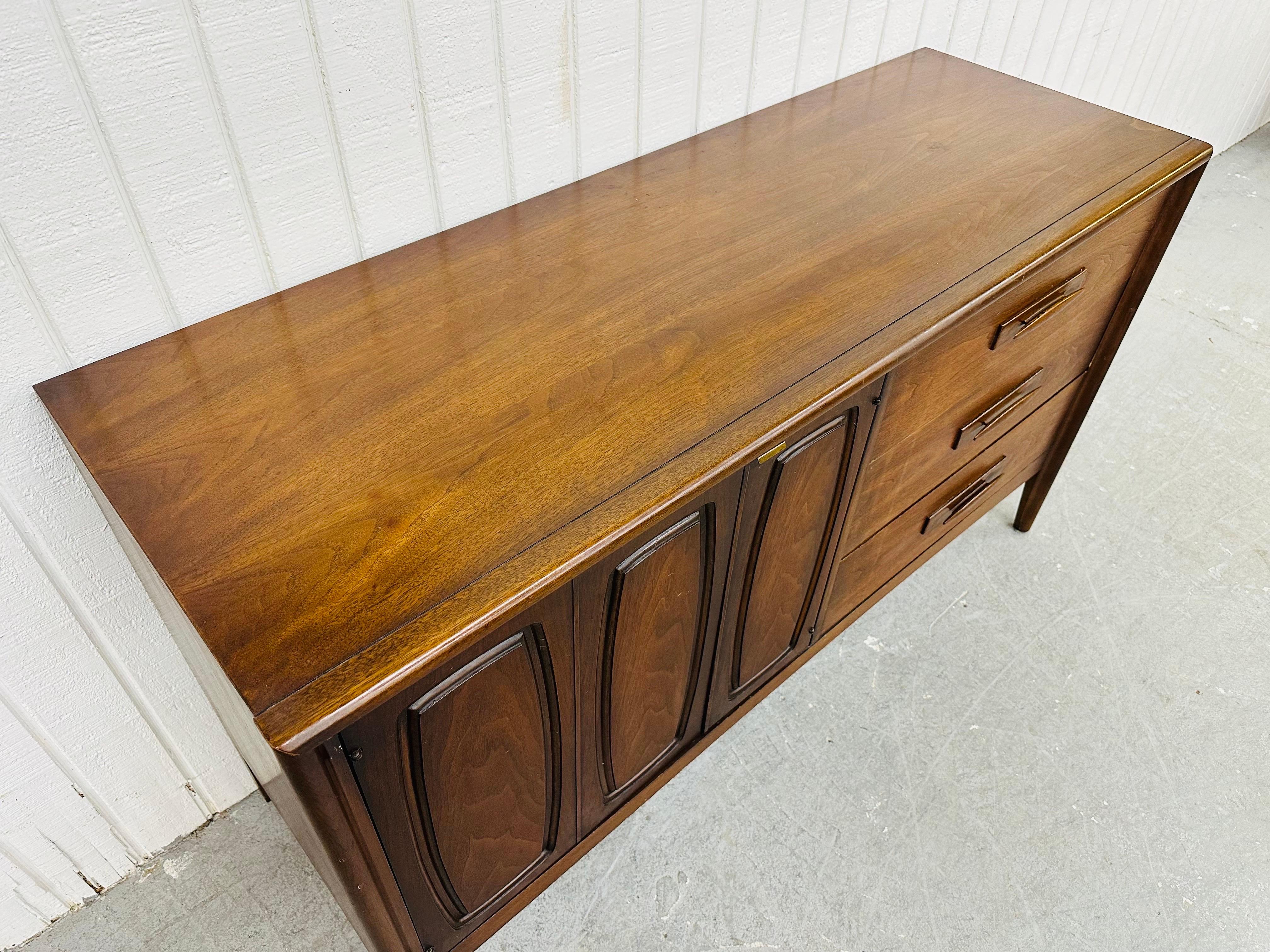 This listing is for a Mid-Century Modern Broyhill Emphasis Walnut Sideboard. Featuring a straight line design, two doors with the iconic Emphasis design that open up to storage space, three drawers on the right with sculpted wooden pulls, modern