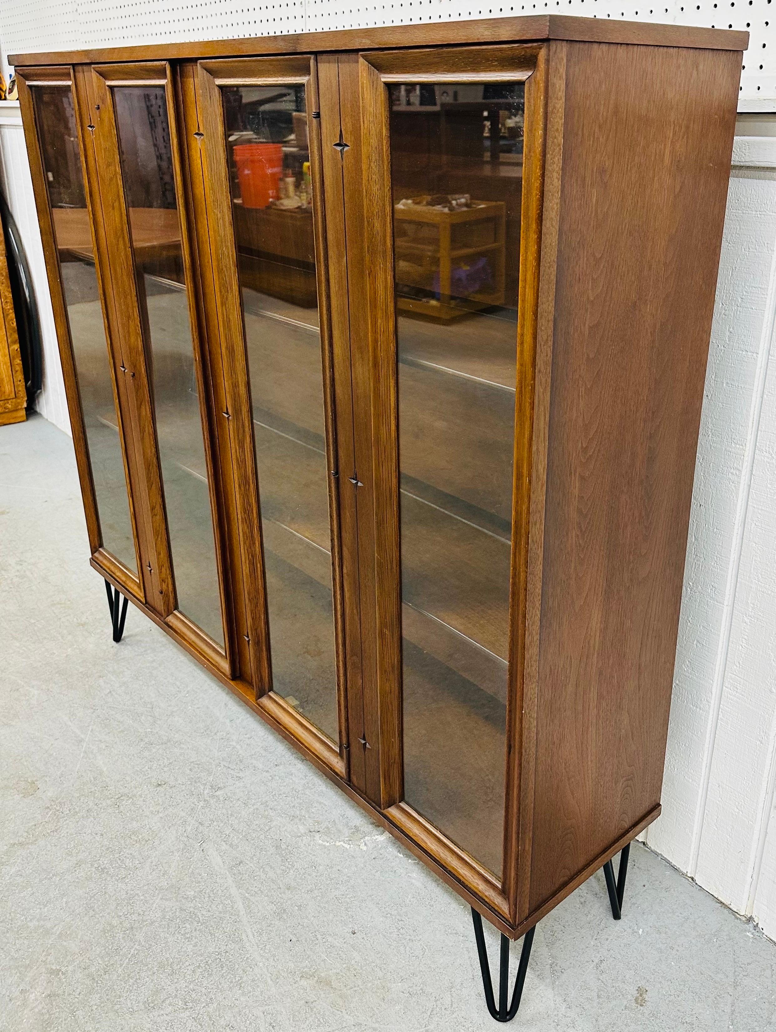 This listing is for a Mid-Century Modern Broyhill Saga Walnut Bookcase. Featuring a straight line design, iconic Saga stars, four glass panels for display, two center doors that open up to storage space, black hairpin legs, and a beautiful walnut