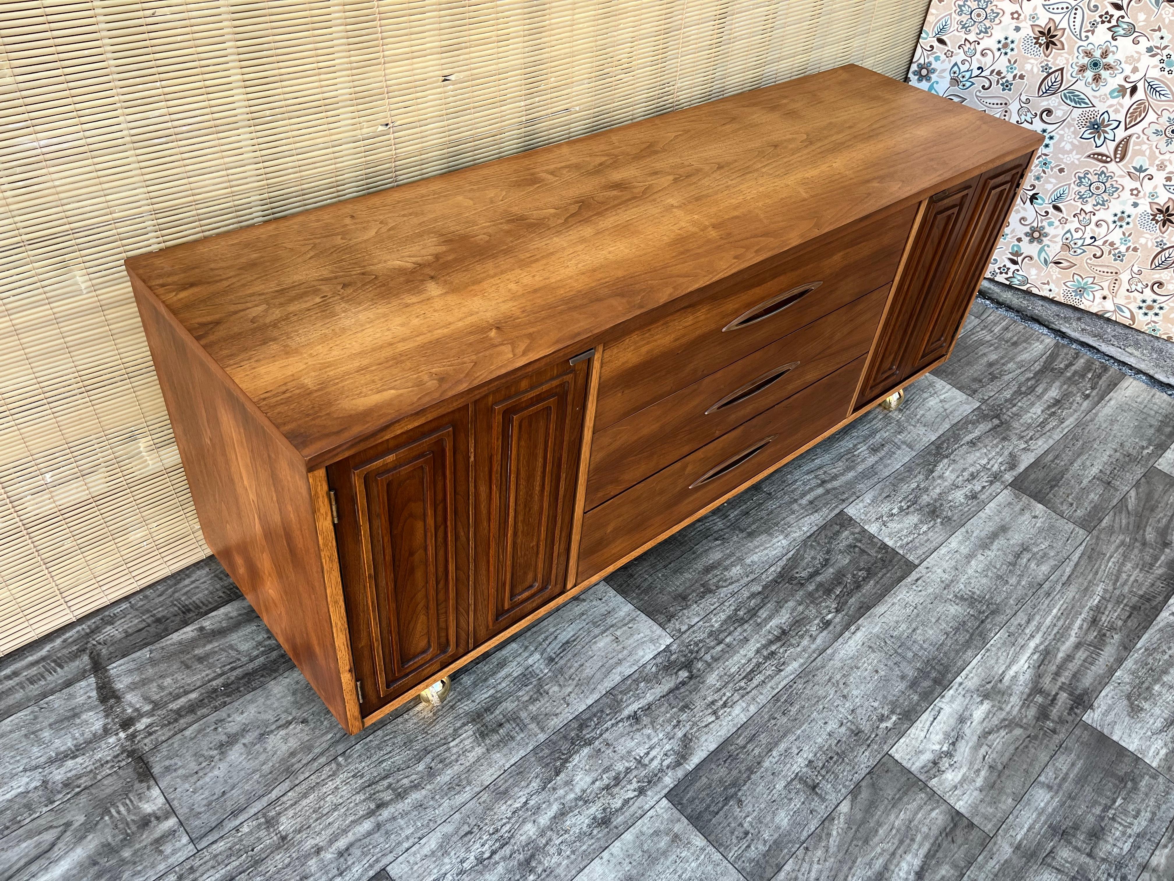 Credenza/buffet Broyhill sculptra, vintage, metà del secolo scorso. Circa anni '60 
Il design moderno di metà secolo è caratterizzato da una bellissima venatura del legno di noce, 3 cassetti con incastri a coda di rondine e 2 ante laterali con