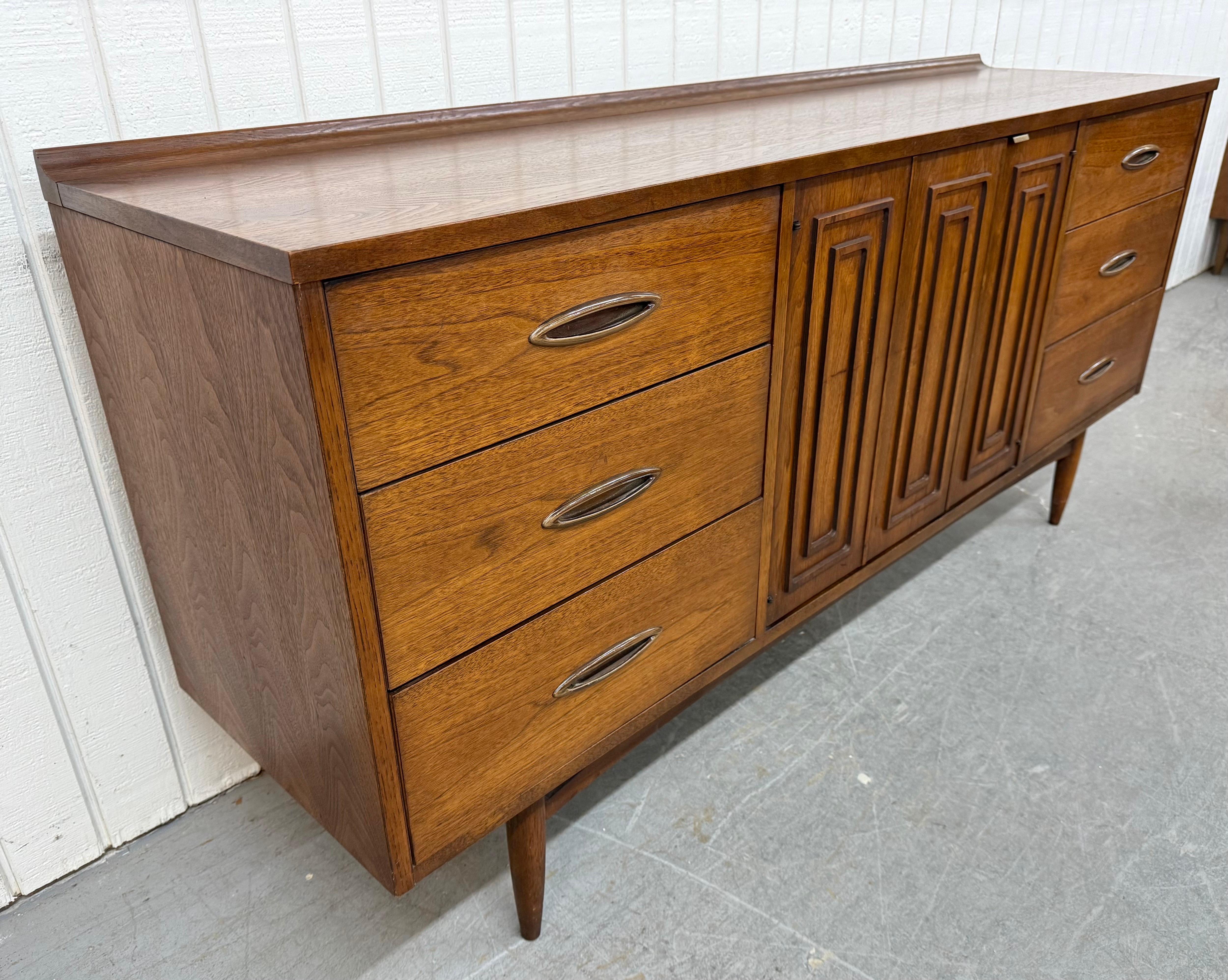 This listing is for a Mid-Century Modern Broyhill Sculptra Walnut 9-Drawer Dresser. Featuring a straight line design, three drawers on each side with original pulls, center doors that open up to three hidden drawers, modern legs, and a beautiful