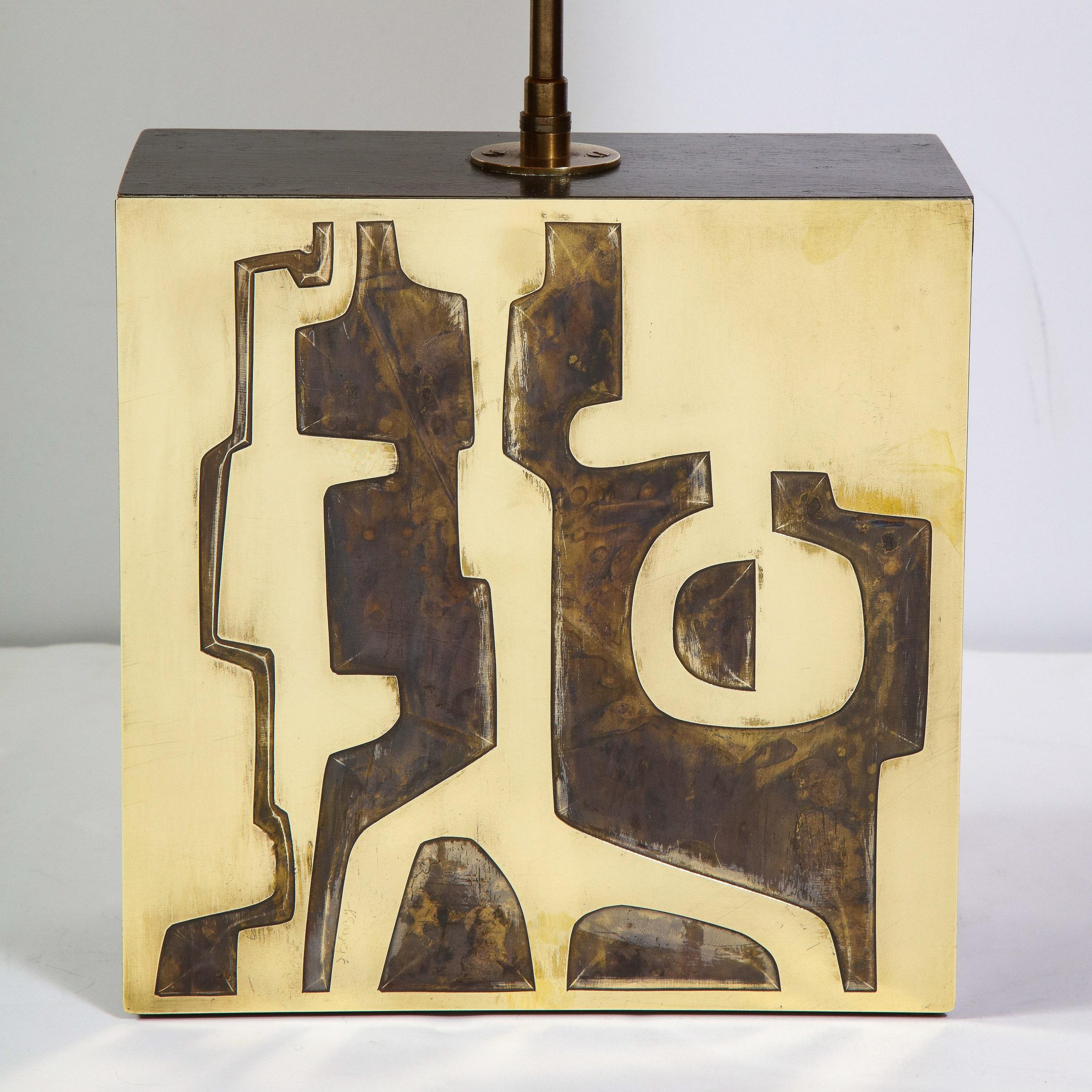 This refined Mid-Century Modern Brutalist brass lamp was realized in the Untied states, circa 1960. It offers a volumetric rectangular body with an abstract petroglyphic design etched in the surface. The vellum lamp shade has been hand painted by