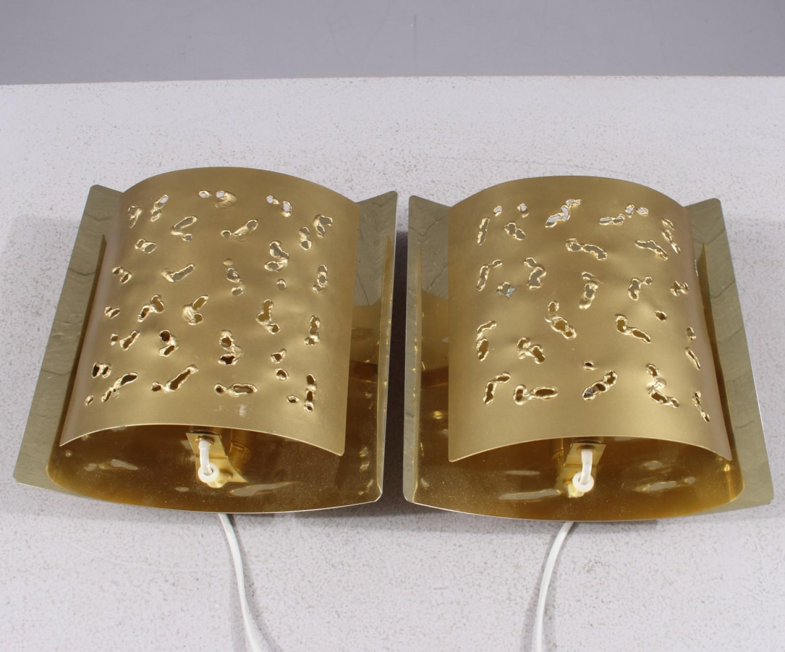 Un'impressionante coppia di lampade da parete o applique di Boréns, realizzate negli anni '70. Progettati in un accattivante stile brutalista, questi apparecchi sono realizzati in ottone e presentano paralumi organicamente perforati che producono un