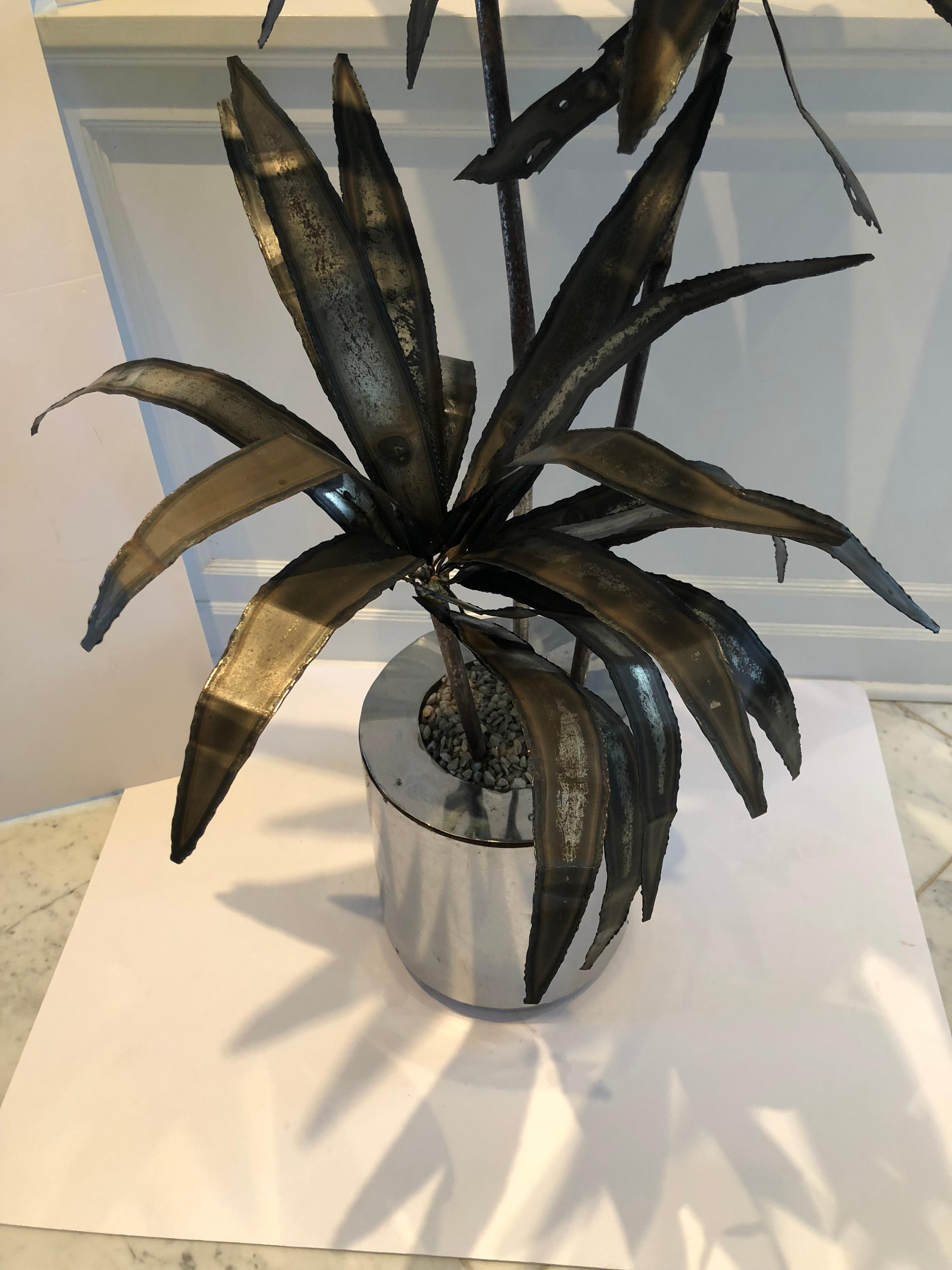 A very chic torch cut sculpture of a palm tree in a pot with pebbled mulch. Definitely midcentury, the sculpture has no signature although it is similar to others by Curtis Jere for Artisans house. The palm leaves are fabricated from pieces of metal