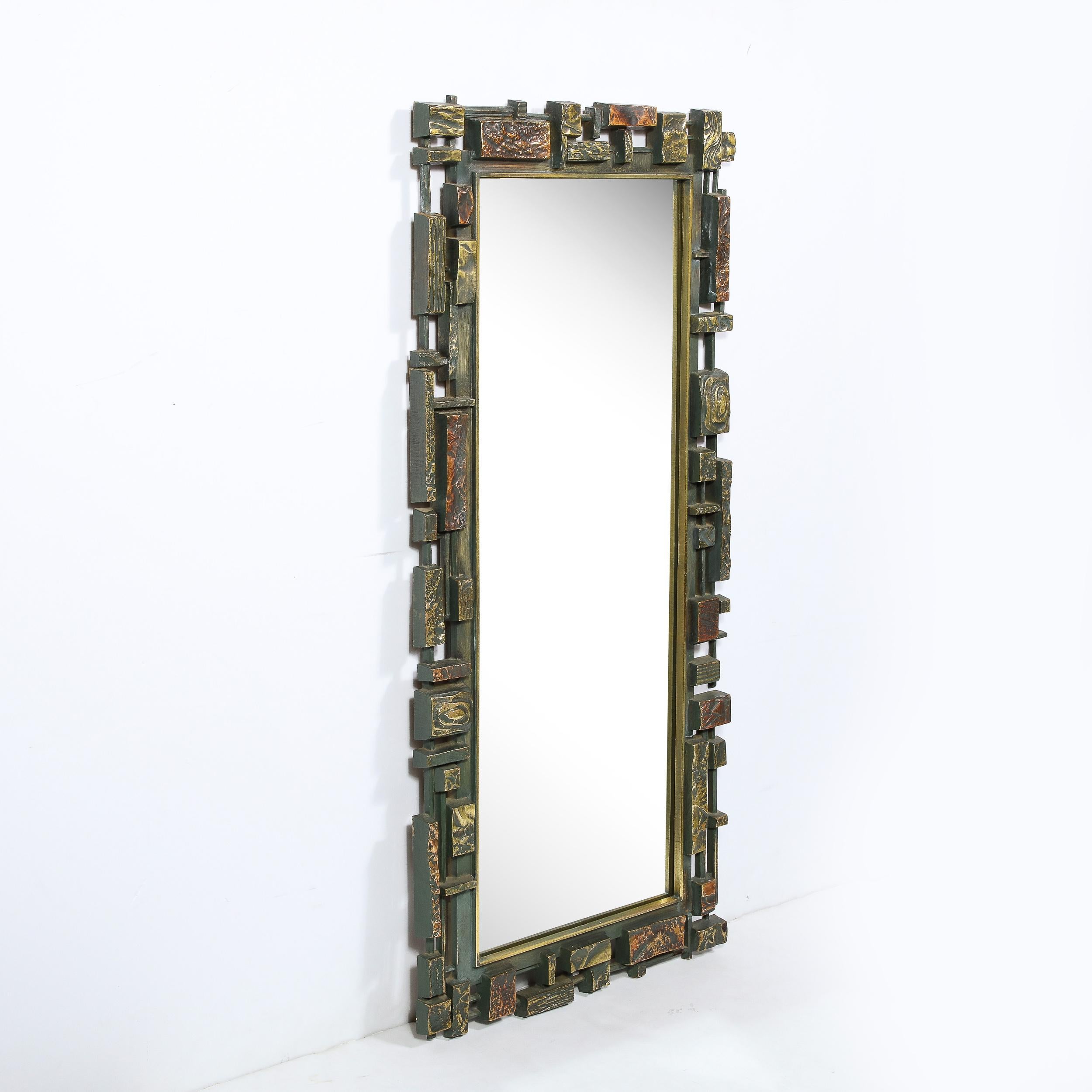 This graphic and sophisticated Mid Century Modern mirror was realized in the United States circa 1970. It features a rectangular plain mirror center surrounded by a mosaic of bronze and copper rectilinear forms presented at staggered heights and