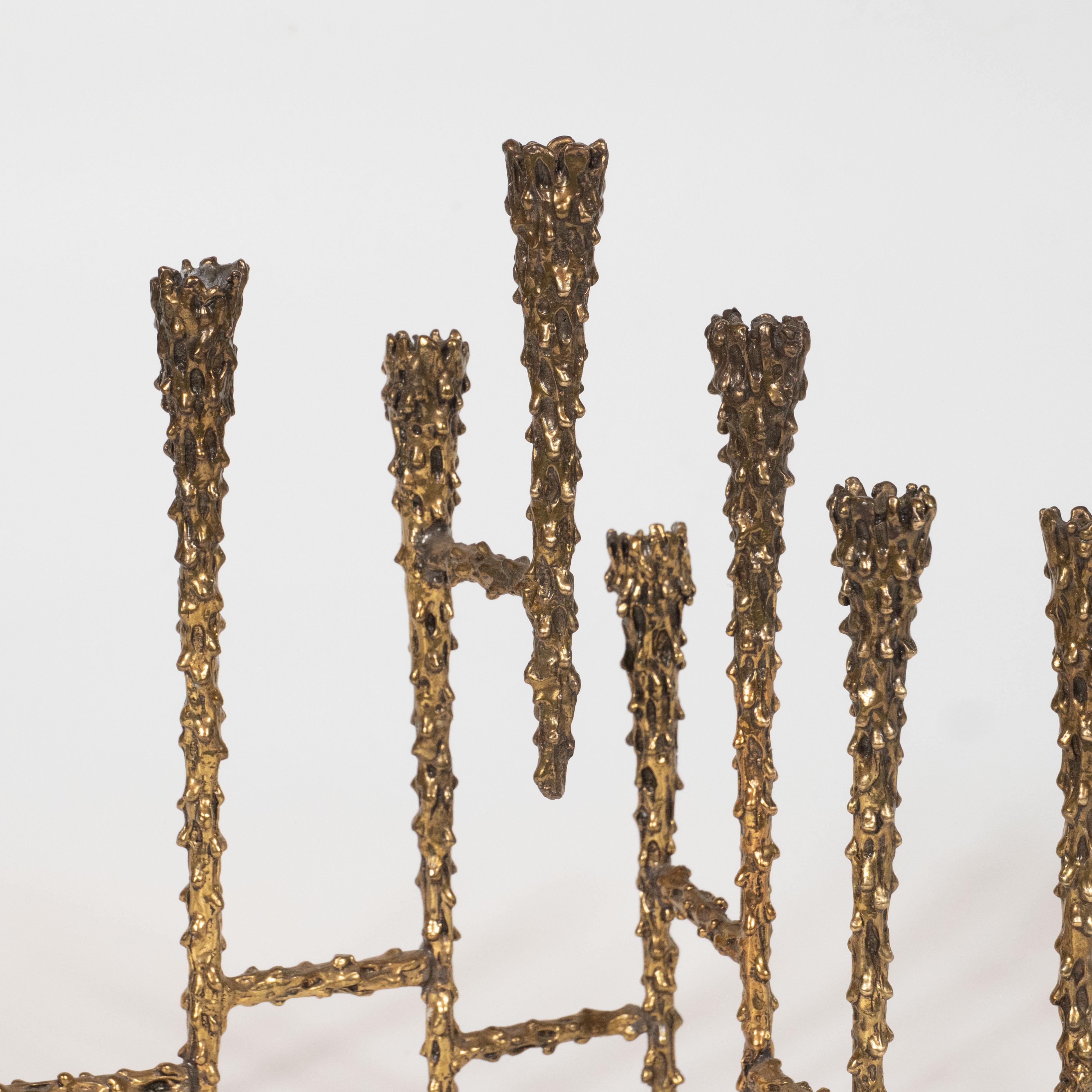 This refined menorah was realized in the United States, circa 1970. It features six tapered candlesticks connected by cylindrical embellishments all with heavily textural skin resembling melting wax. With its sophisticated brutalist aesthetic, this