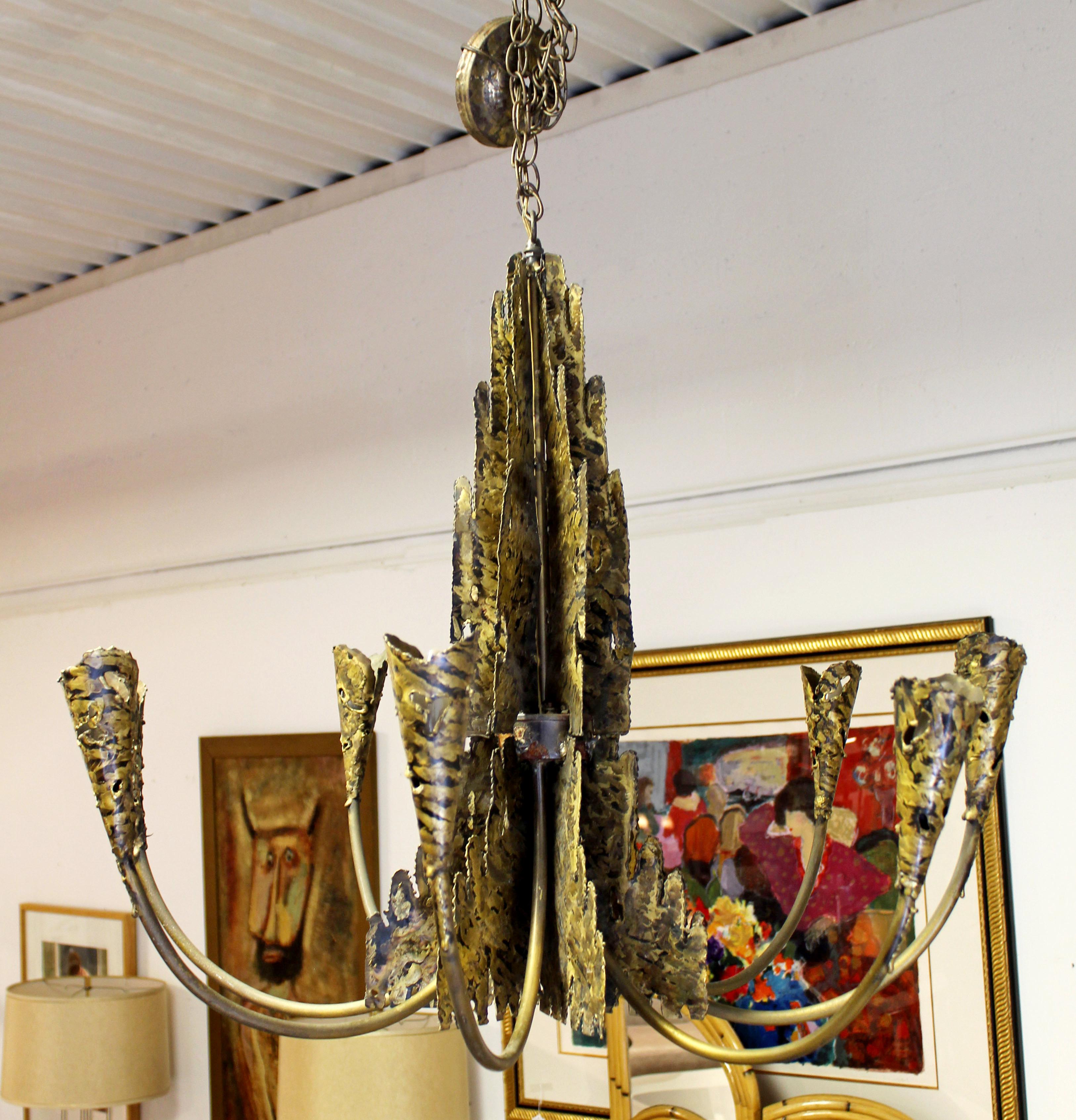 For your consideration is an incredible, torch cut brass, Brutalist, chandelier light fixture, with eight arms, in the style of Tom Greene or Paul Evans, circa 1960s. In excellent condition. The dimensions are 35