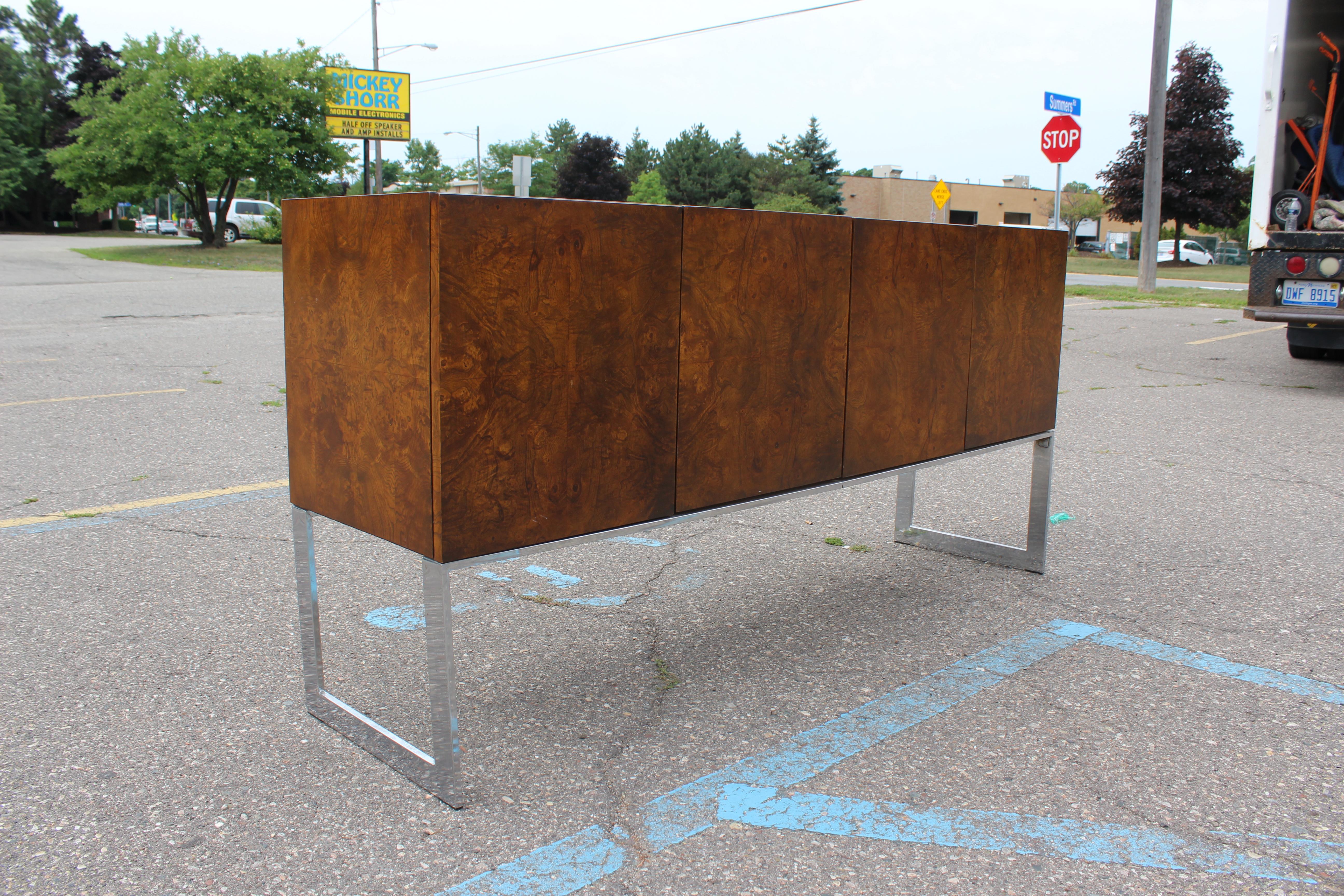 For your consideration is a sideboard by Milo Baughman is composed of a stunning burl wood cabinet that is set on a light chrome frame. One half of the sideboard features adjustable shelving, while the other half features two cutlery drawers and