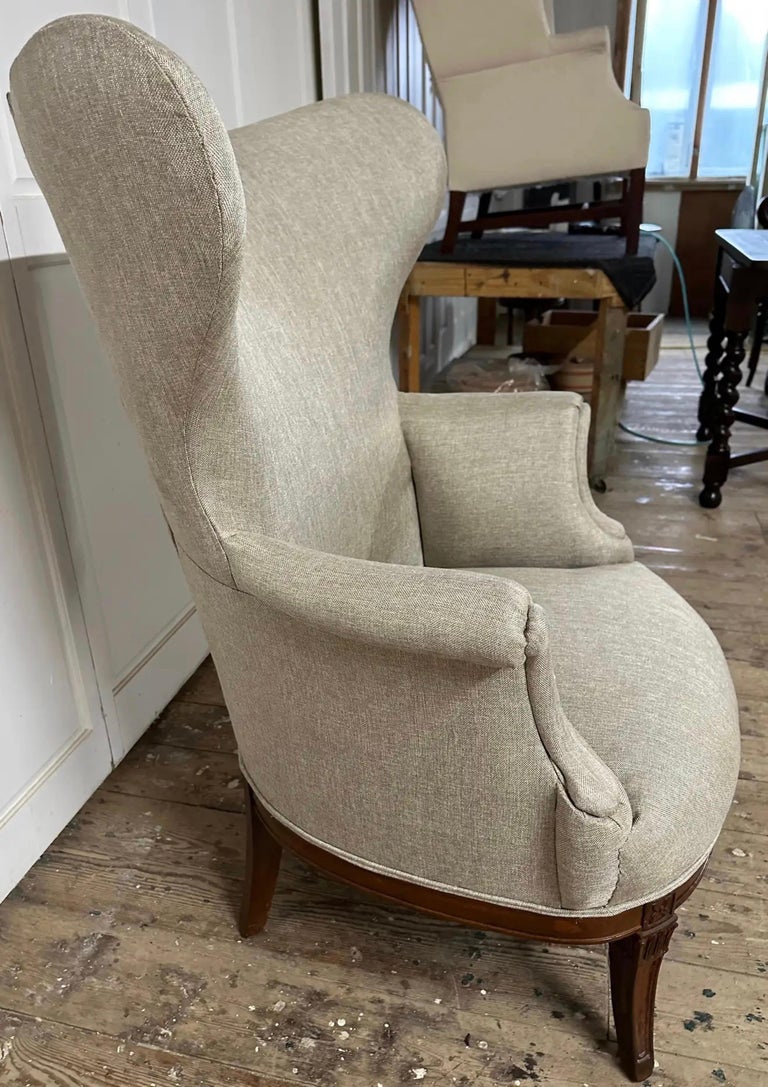 In the style of Paolo Buffa, this 1950;s butterfly wing back chair has been restored and newly upholstered in a neutral linen fabric. Beautifully carved wood swag motif accents the front of the chair leading down to gracefully outward curved tapered