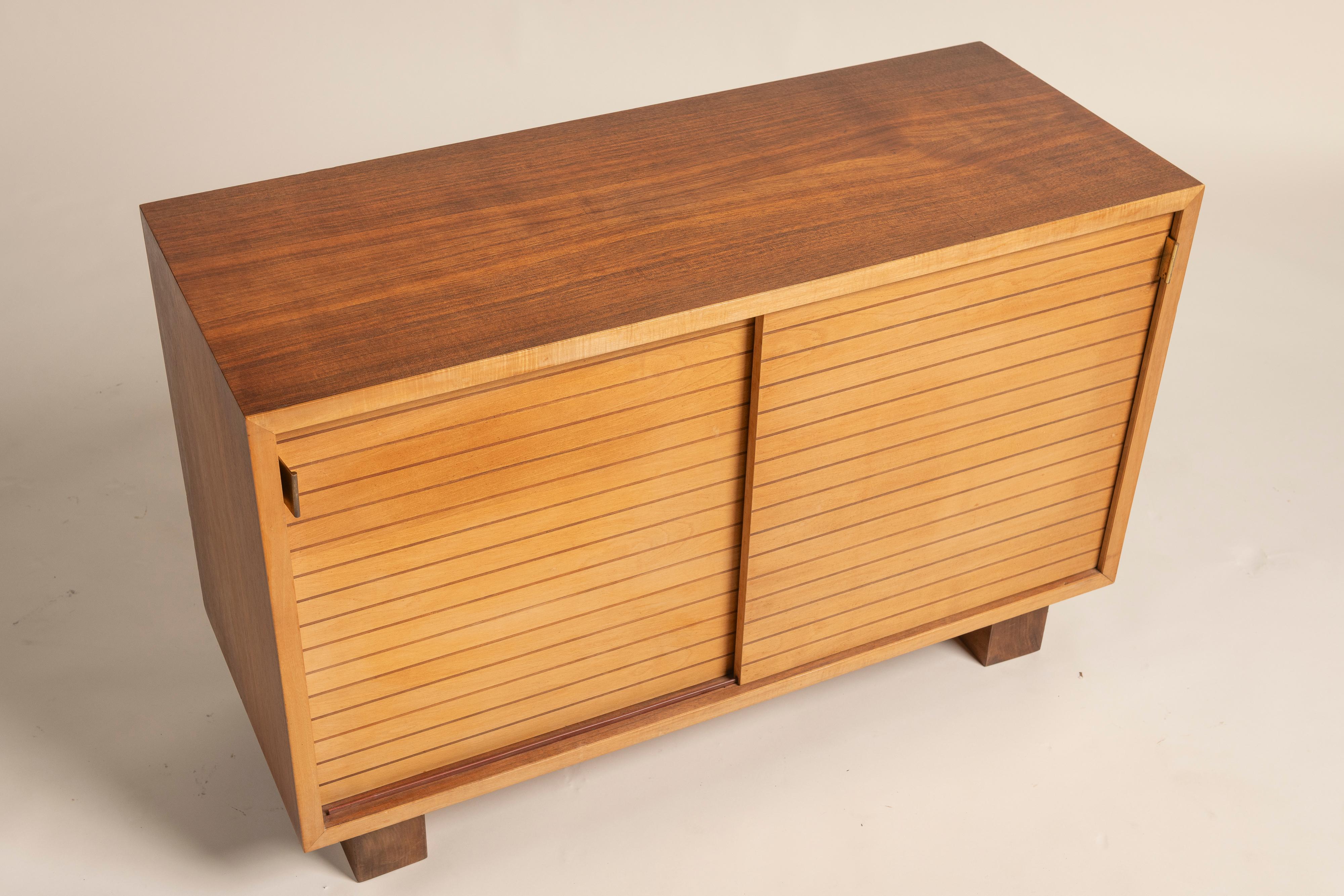 Este armario moderno de mediados de siglo presenta un elegante diseño de puertas correderas de lamas, que revela un interior bien organizado. Fabricada en madera de tonos cálidos, la pieza se asienta sobre robustas patas ligeramente cónicas. El