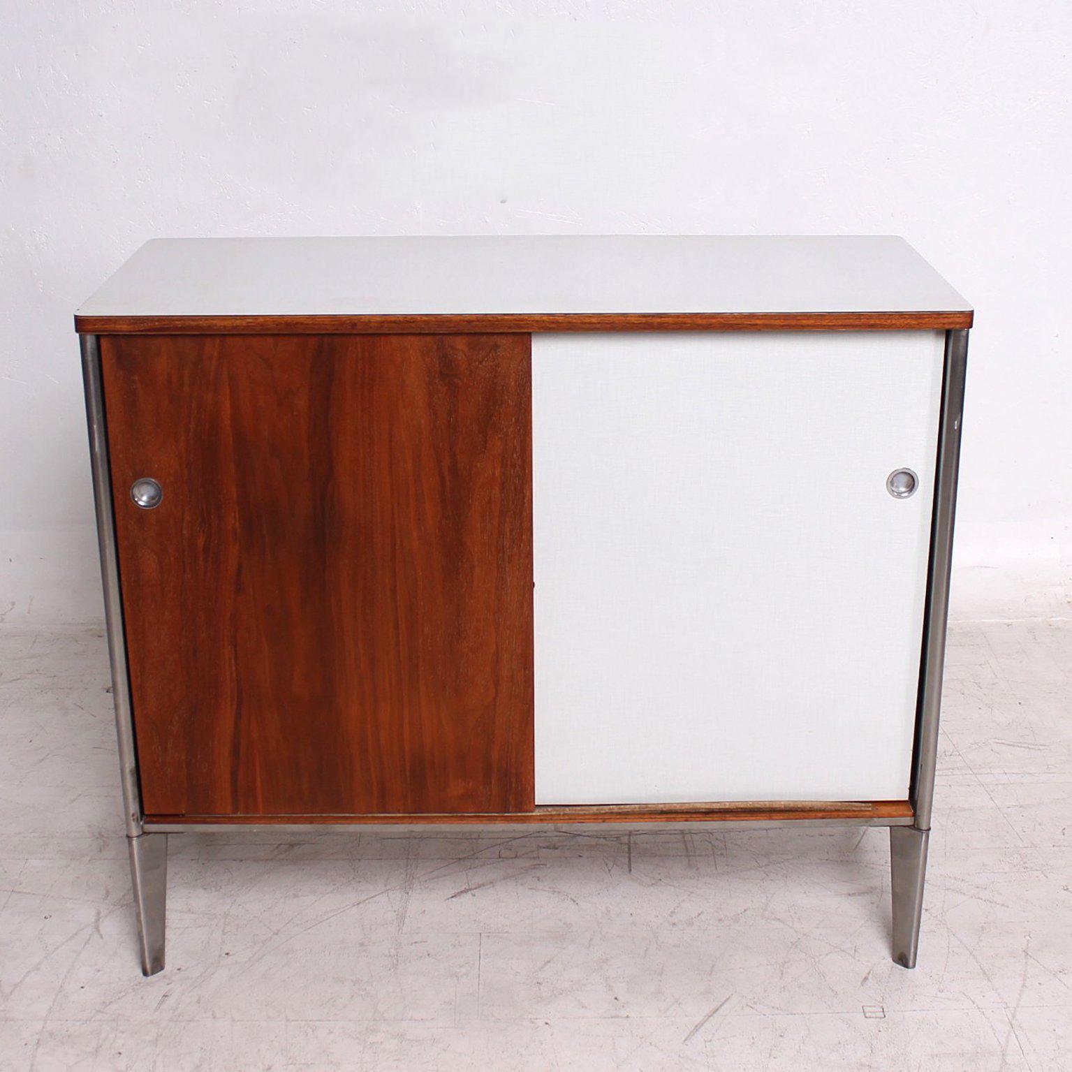 For your consideration a vintage Mid-Century Modern cabinet made of walnut plywood, stainless steel legs in sculptural tapered finish and light gray formica with a grid pattern graphics. 
The interior is painted in light green color and features two