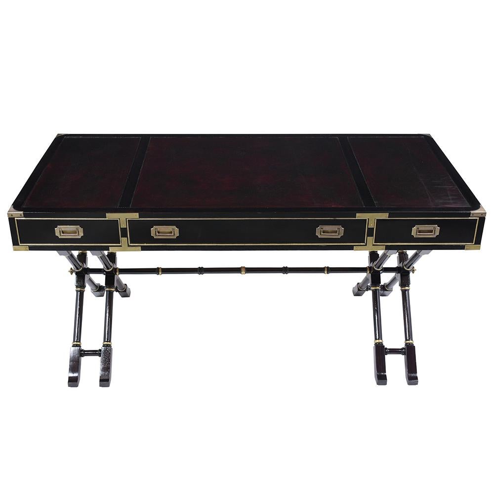 A Mid-Century Modern Campaign desk handcrafted out of mahogany wood stained in a rich ebonized lacquered finish and features its original leather top newly dyed in a dark burgundy color with a beautiful patina finish. This eye-catching desk has a
