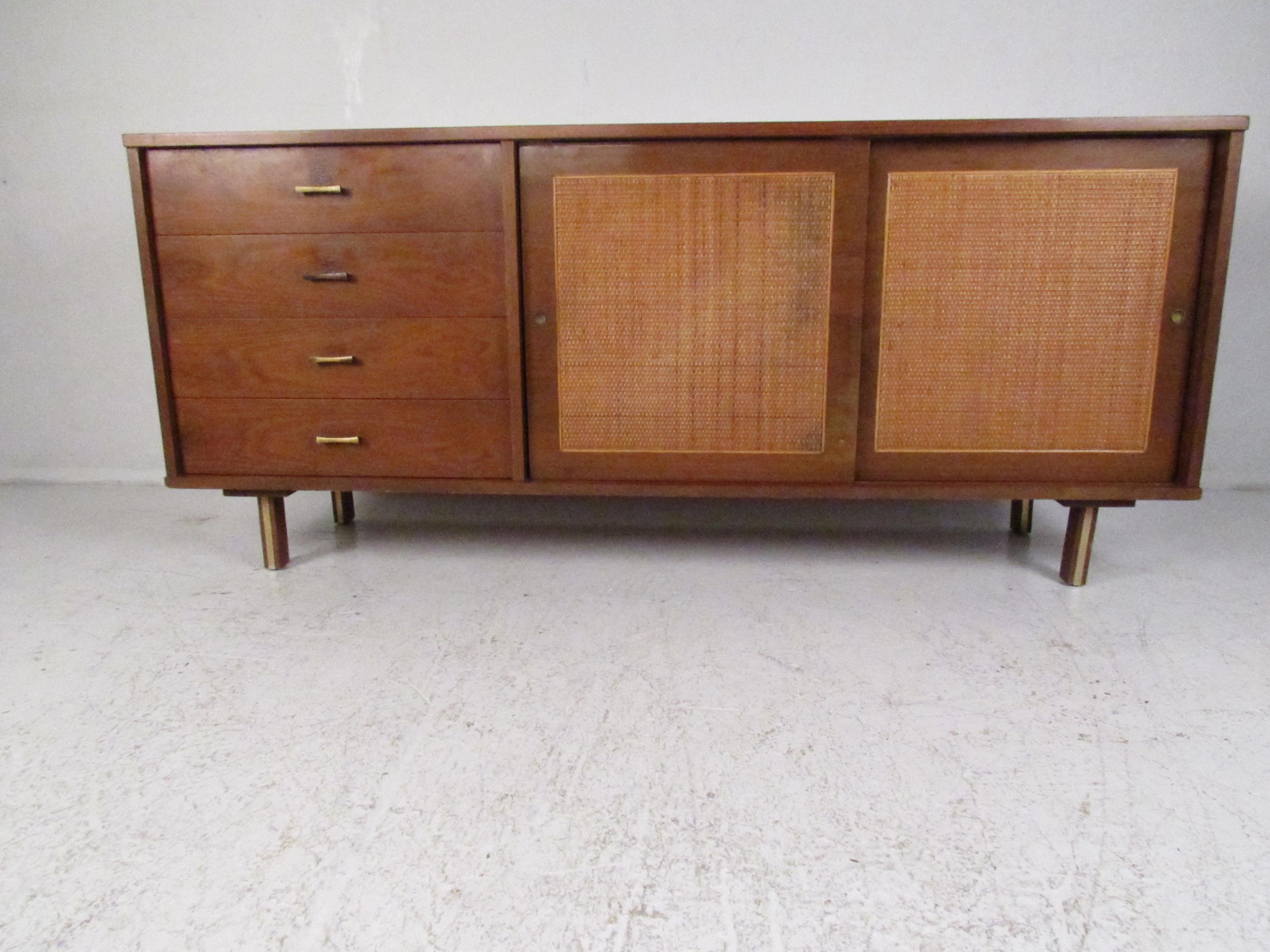 A beautiful vintage modern sideboard with woven cane front sliding doors and four hefty drawers. The circular recessed brass cabinet pulls and sculpted brass drawer handles show quality craftsmanship. This sleek mid-century case piece has unusual