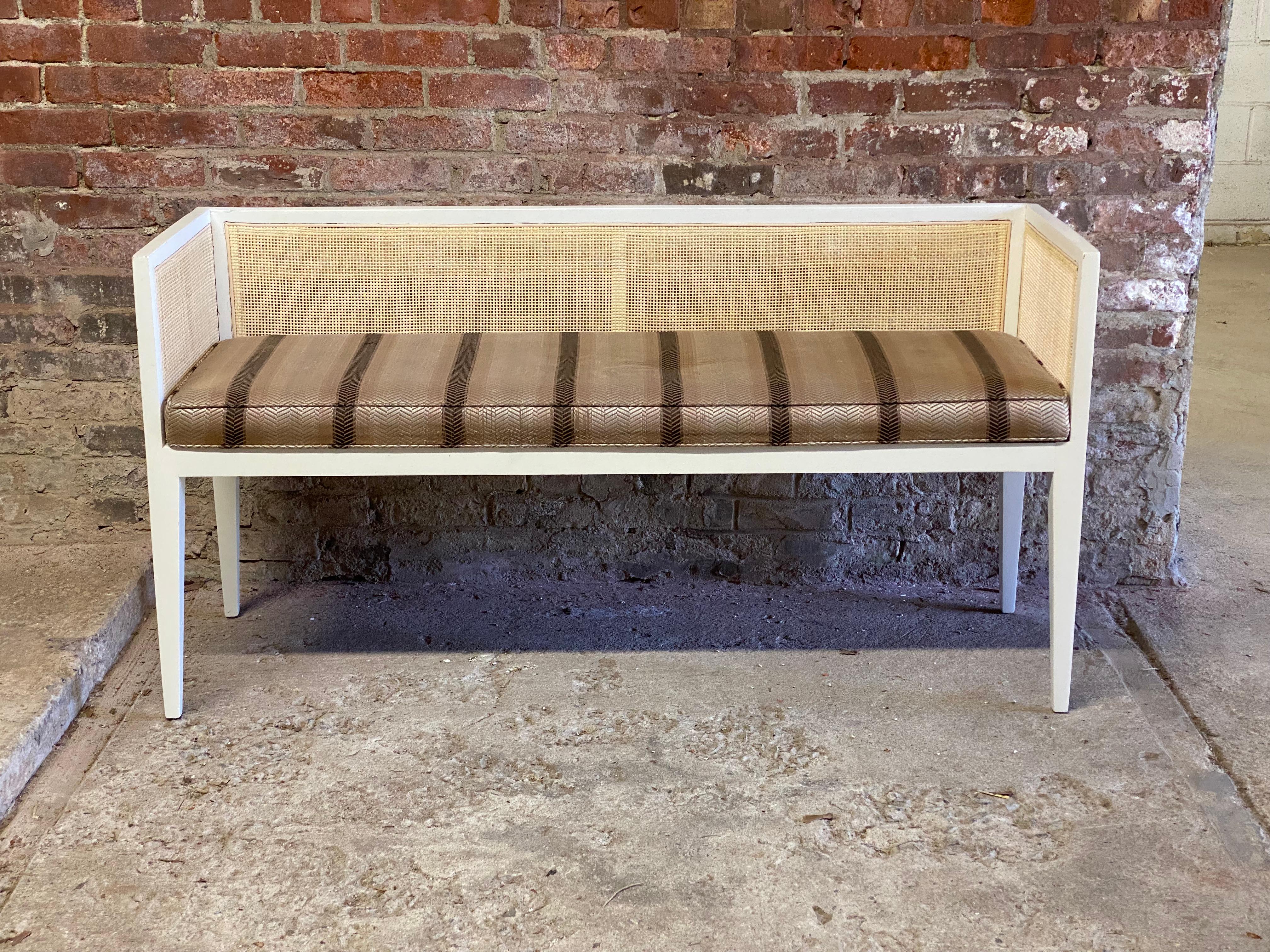 Caned back and upholstered bench. Circa 1960-70. Newly caned back with an upholstered drop in seat. Featuring older custom white finish with tapered legs and level arm and back support. A wonderful addition to the foyer, hallway or underneath a