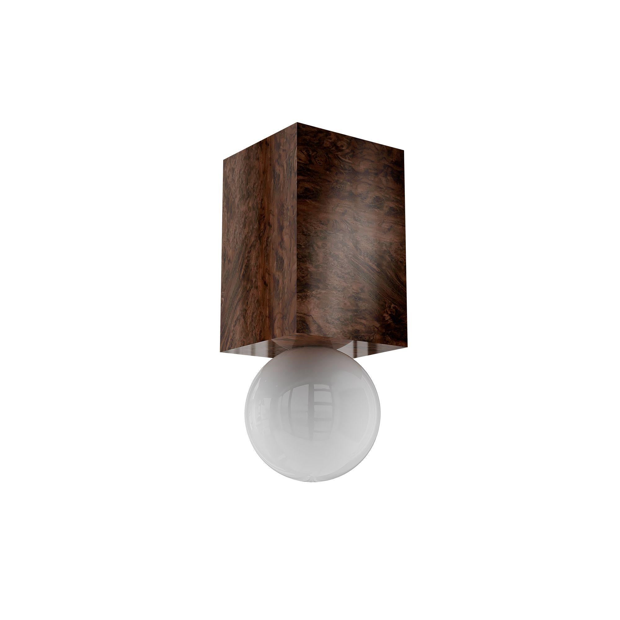 La lampada a sospensione Athena Wood porta l'eleganza minimalista a nuovi livelli, combinando una struttura in legno scuro con linee architettoniche pulite. Ispirata all'estetica brutalista, la sua composizione scultorea offre un contrasto caldo e