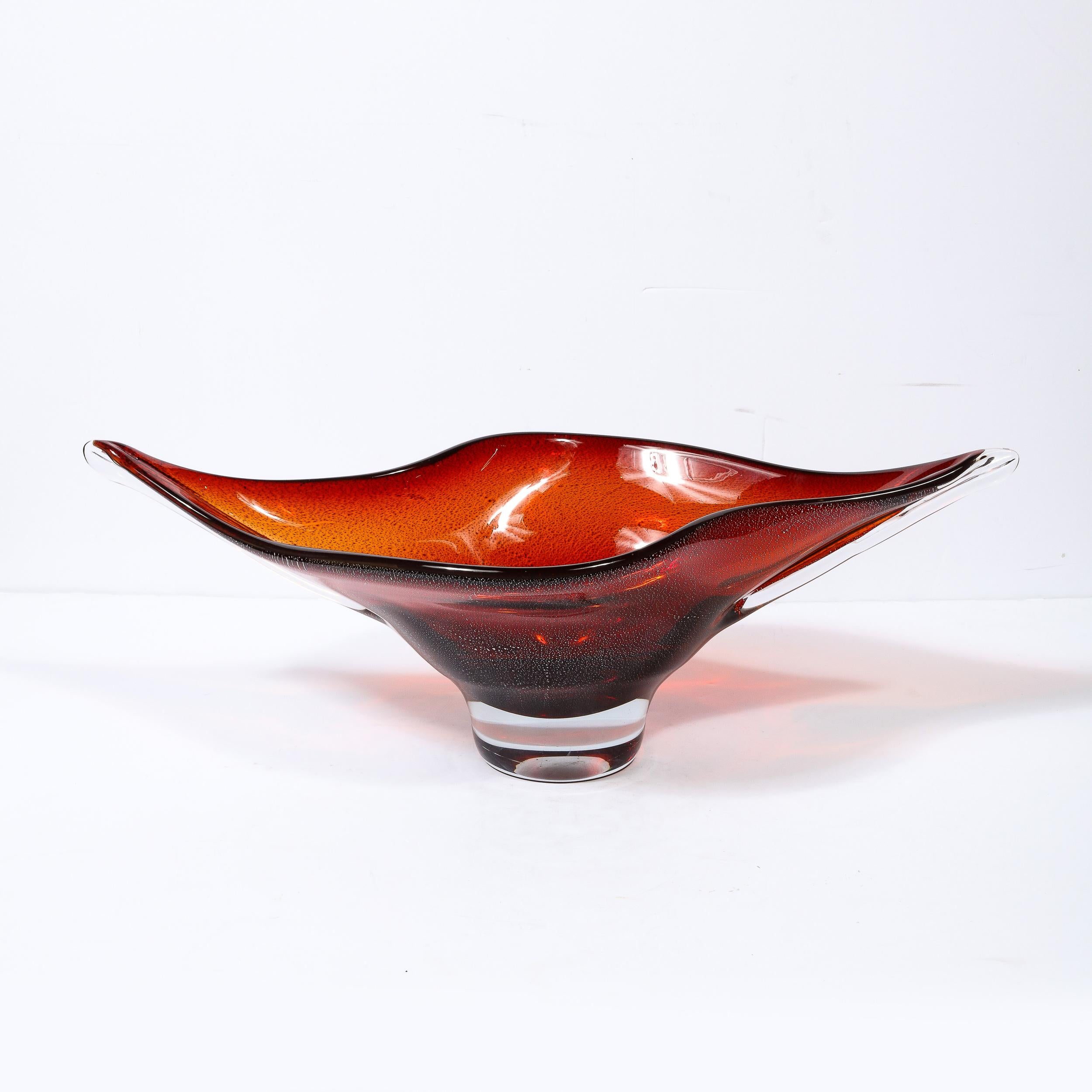This stunning Mid-Century Modern centerpiece bowl was realized in Murano, Italy- the island off the coast of Venice renowned for centuries for its superlative glass blowing- circa 1960. It features an elliptical form with sinuously curved sides and