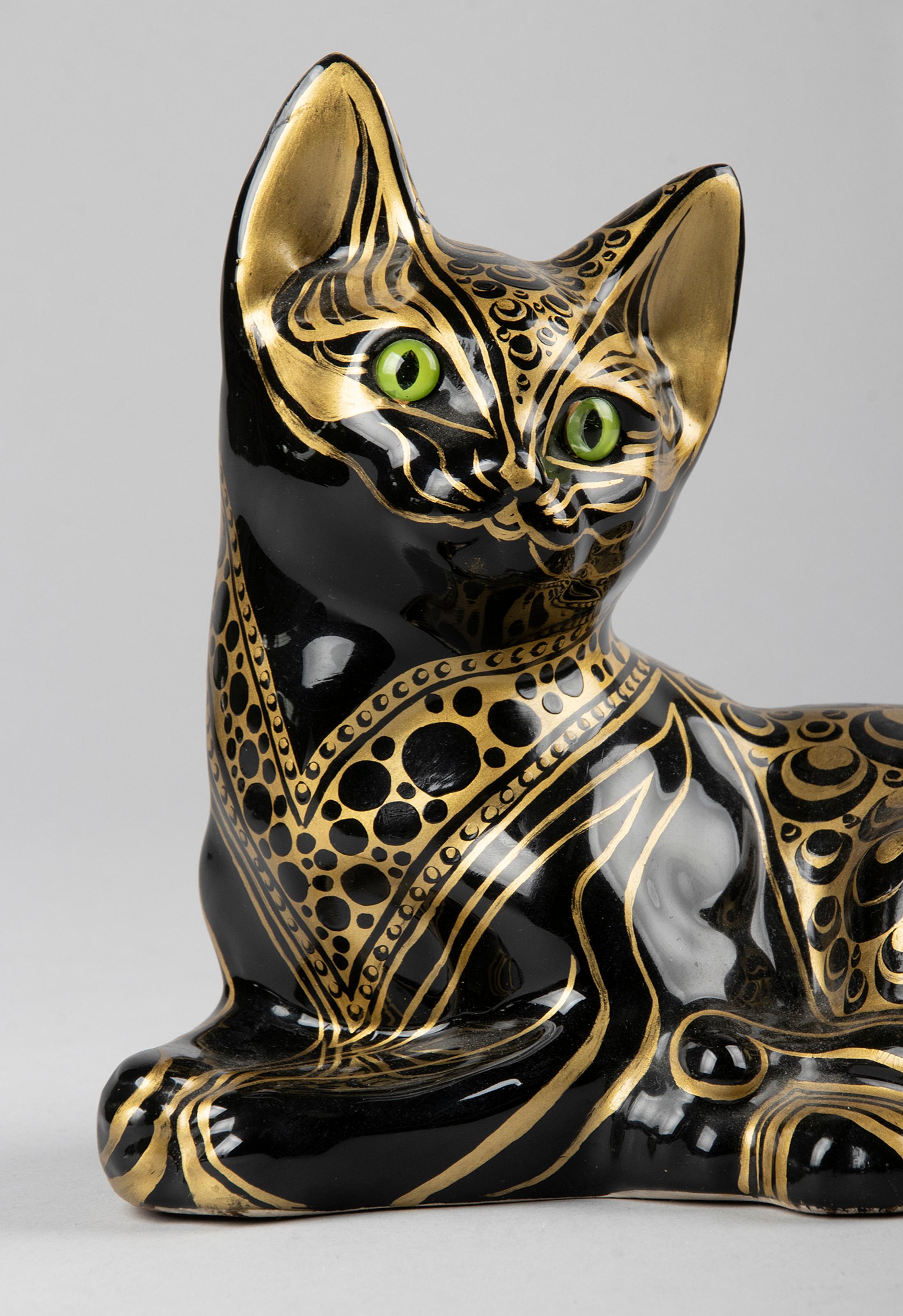Decorative ceramic statue of a black cat. The statue is hand painted with gold accents. The cat has glass eyes. The object is not marked, the maker is unknown.