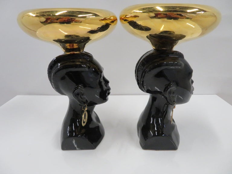 A pair of 1950s ceramic busts of black Nubian Princess figures with gilt bowls on their braided hair heads. With original brass loop earrings, the inside of the gilt bowl glazed in a sky blue. Unmarked as to the maker, they are a rare pair in