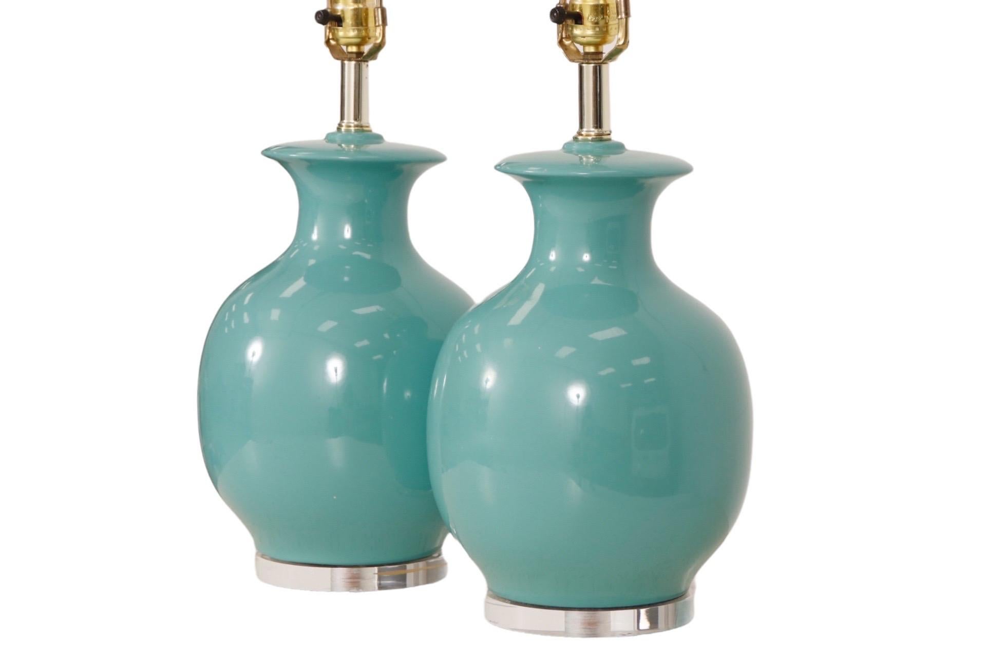A pair of Mid Century Modern ceramic and lucite table lamps. Urn shaped bodies are Tiffany blue above thick round lucite bases. Maker's label underneath reads “US Homes of Florida Rutenburg Homes Division”. Each lamp measures 18.5”H to the top of