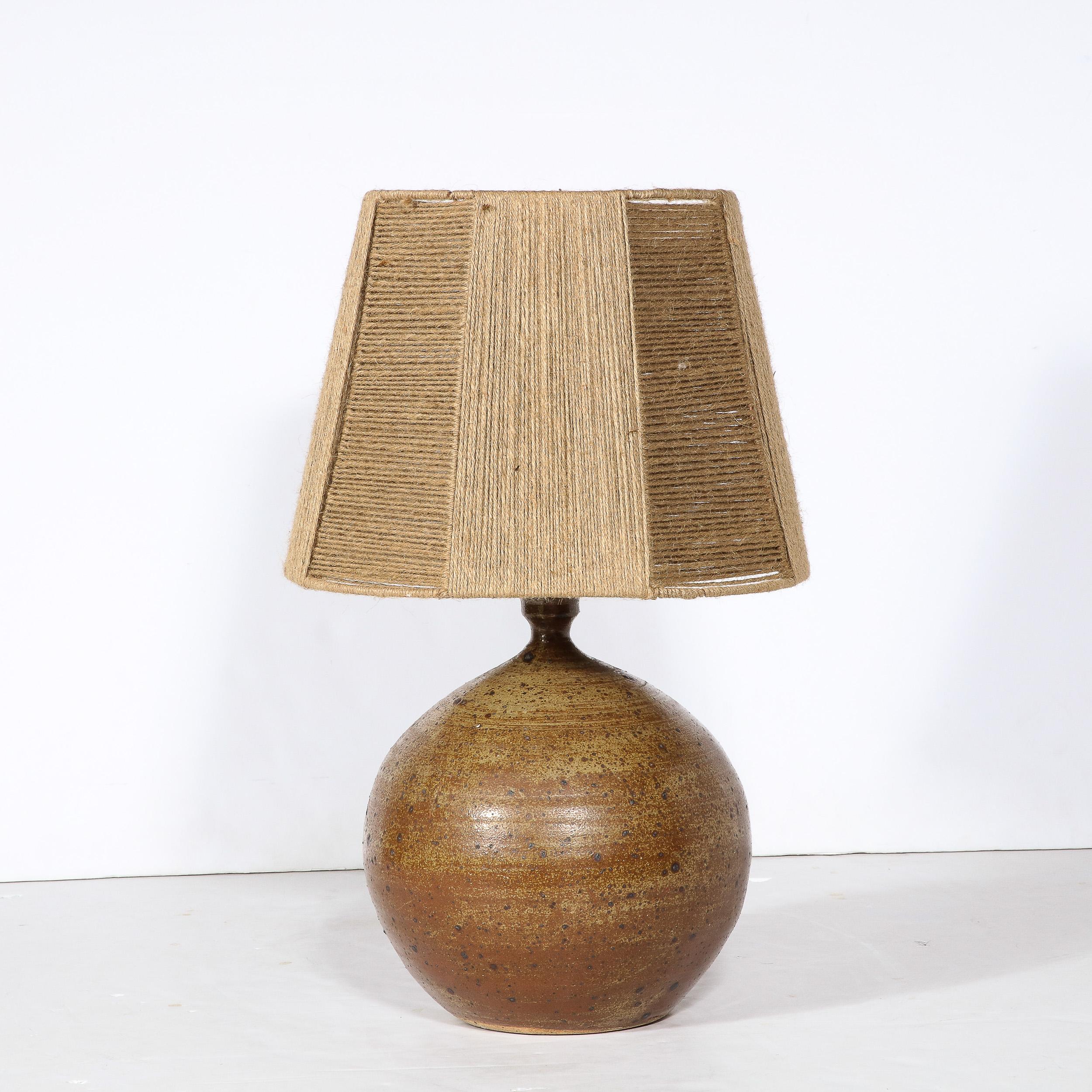 This beautiful and sophisticated Mid-Century Modern ceramic table lamp was realized in France circa 1960. It features a protuberant orbital body with a hand glazed skein in a sumptuous burnt umber hue with expressionistic splashes of dark espresso