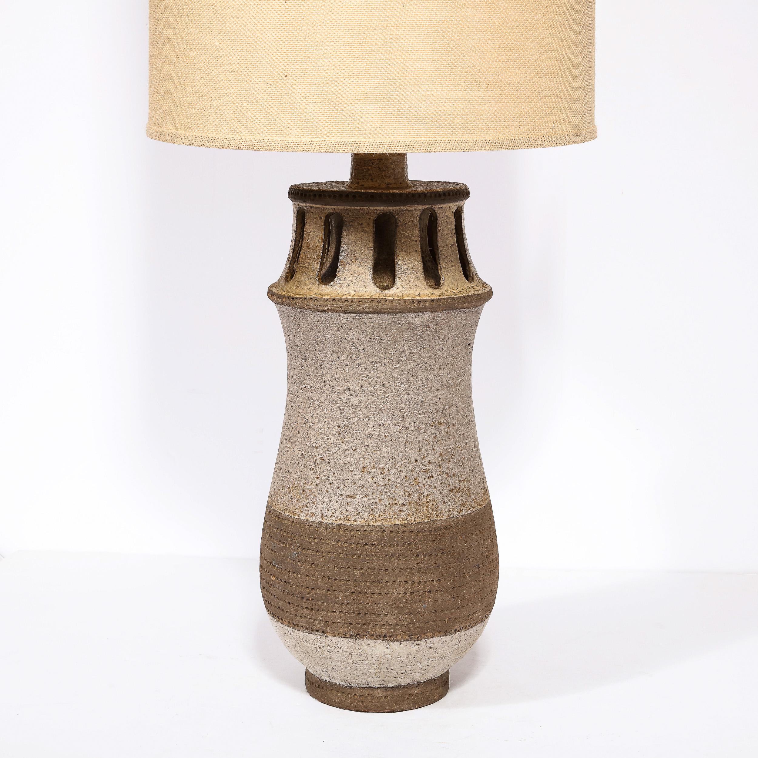 This stunning Mid-Century Modern ceramic lamp was hand crafted in the United States circa 1960. It features an undulating cylindrical body sitting on a circular cafe au lait base. The curved body has been executed in a dark ecru hued textured