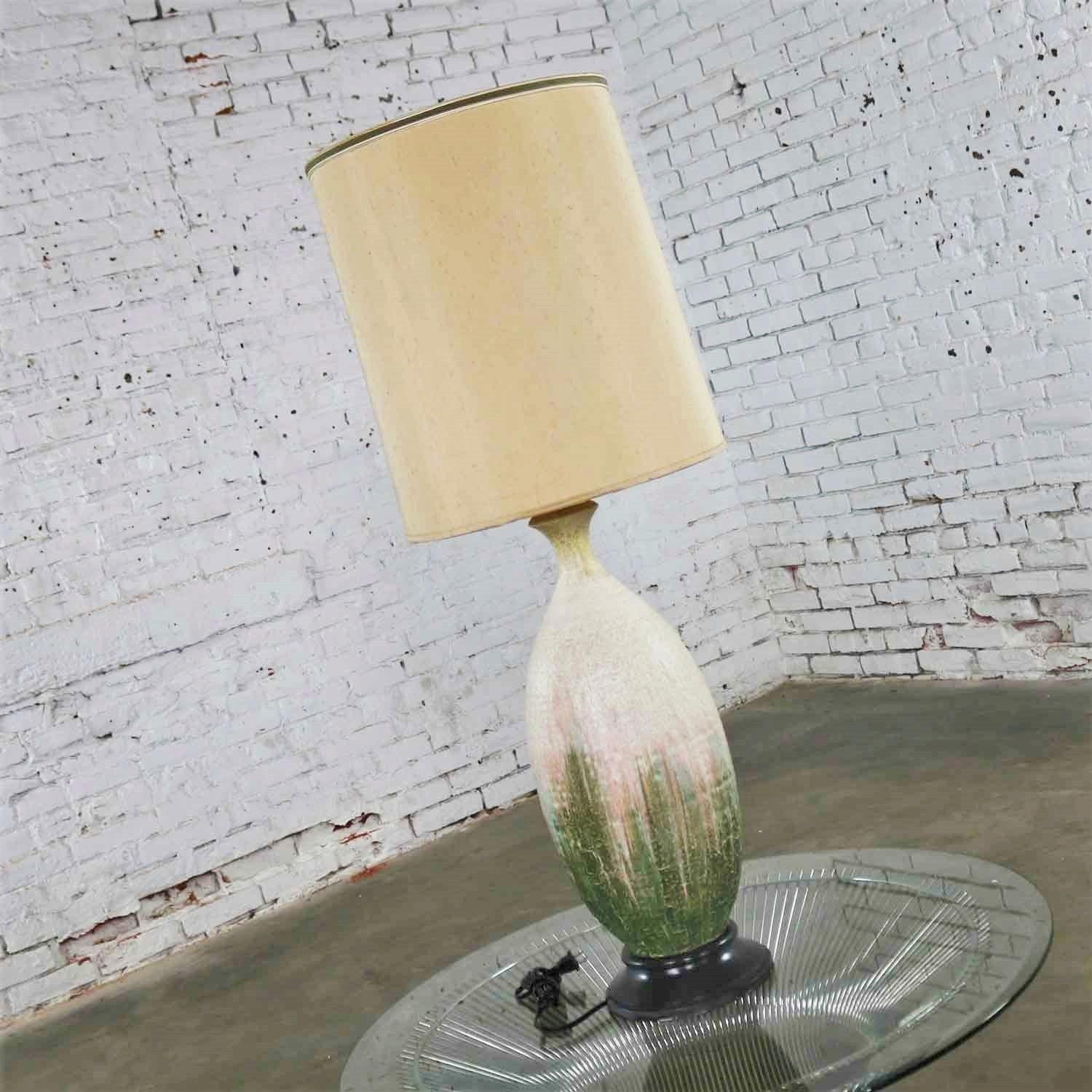 Handsome large Mid-Century Modern ceramic table lamp with a cream, fuchsia, and green lava drip glaze on a wood base. It wears its original hard lined linen look tall drum shade. Both are in wonderful condition. It has been rewired and given a new