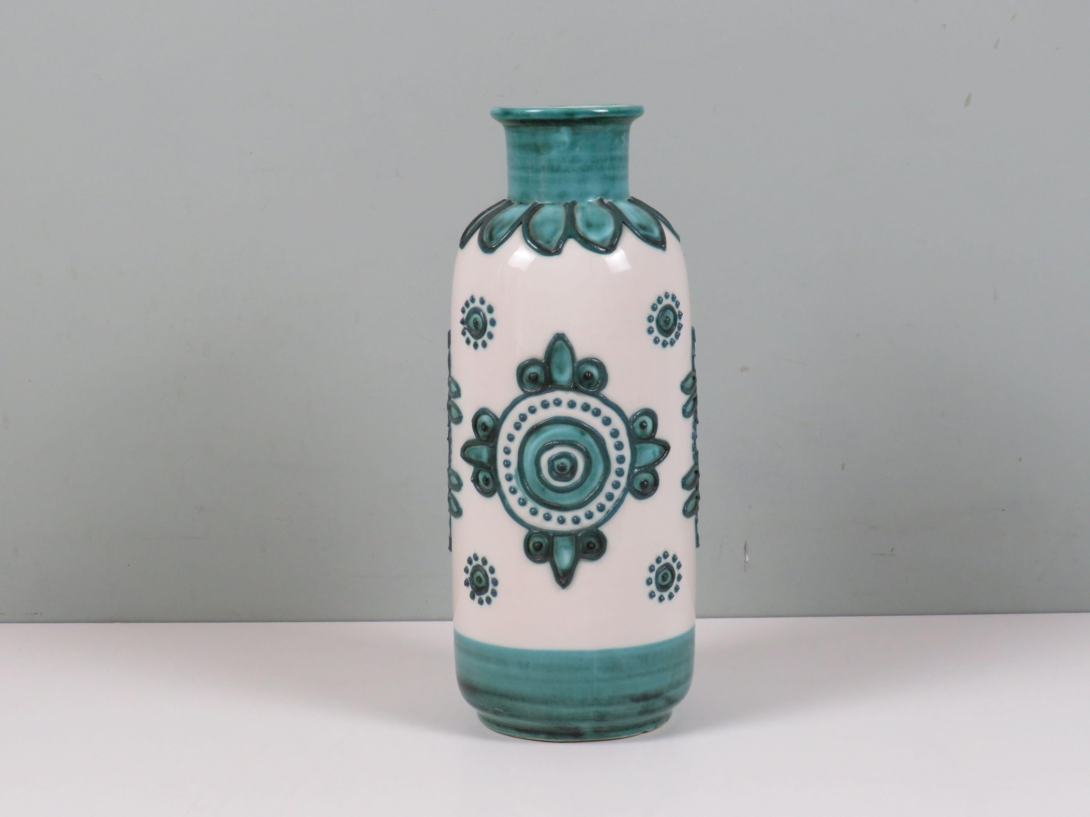 A tall cylindrical ceramic vase with floral relief and vibrant turquoise glaze. Model 407-34, bearing the original Schlossberg Keramik label.

Dimensions: 34 cm height × 15 cm diameter.

This design aligns with the aesthetic language of Bodo Mans,