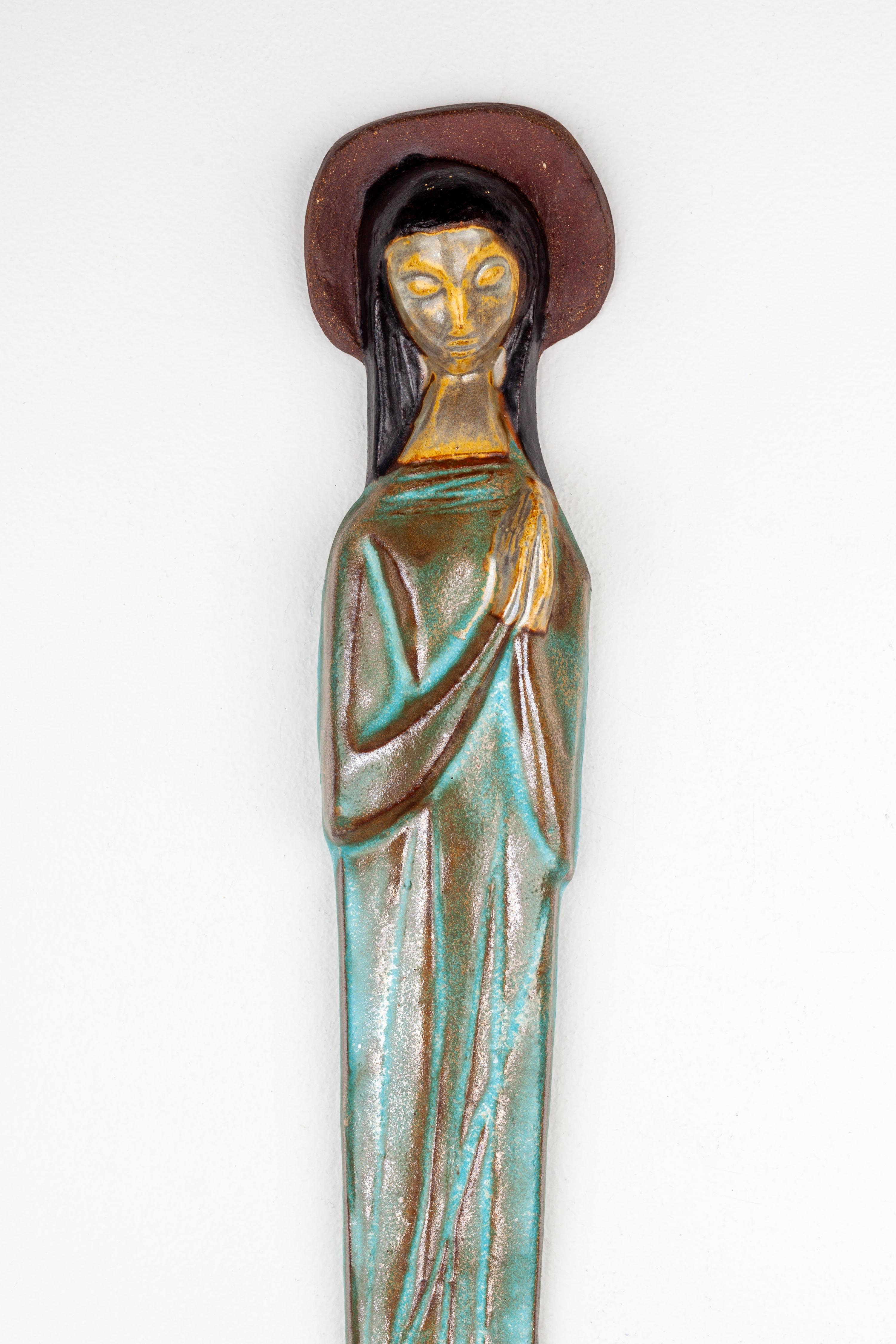 This elegant ceramic representation of the Virgin Mary is a superb example of mid-century modern craftsmanship, hand-formed by a skilled European studio pottery artist. The figure captures Mary in a state of serene contemplation, her posture and