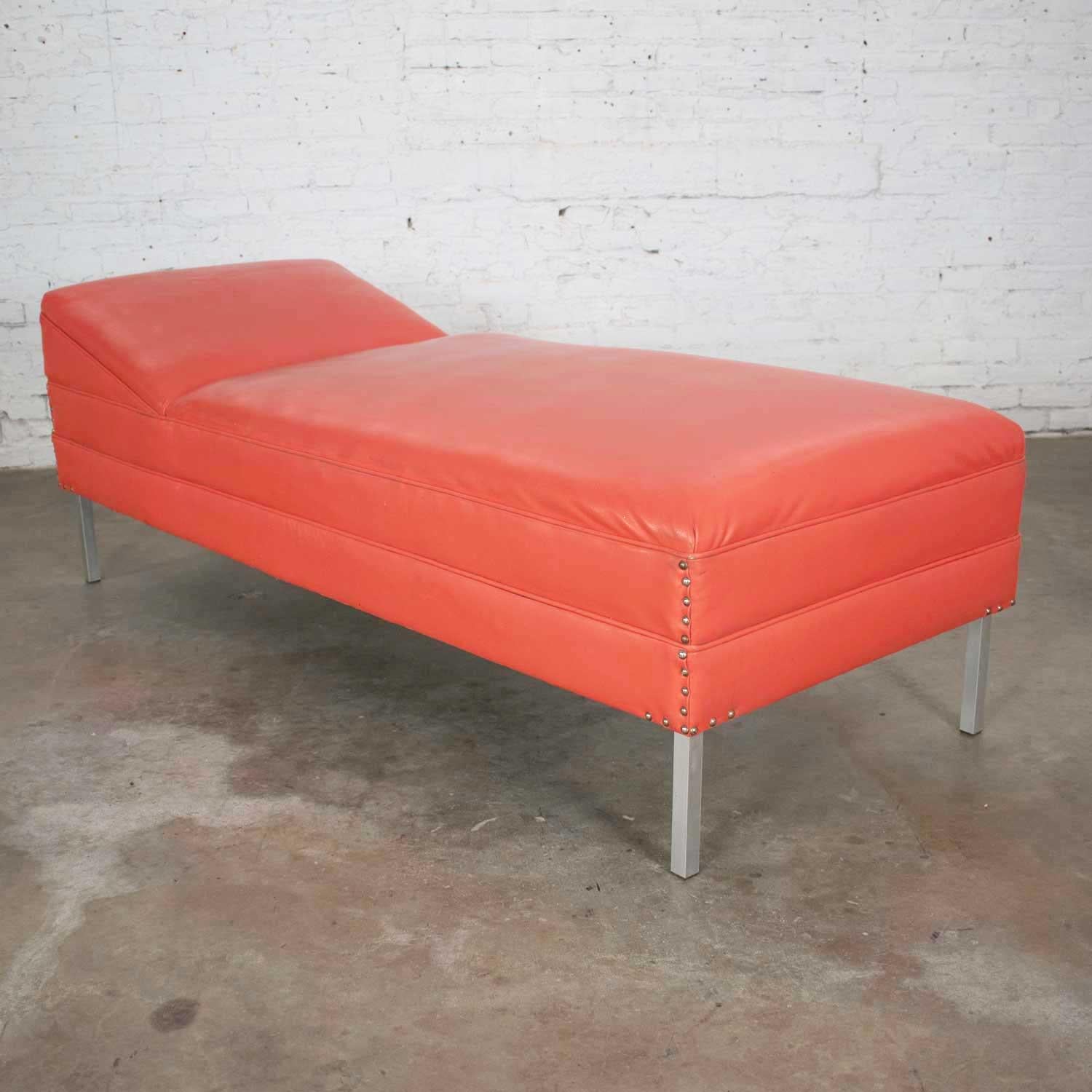 Handsome Mid-Century Modern coral vinyl faux leather and aluminum leg chaise lounge or day bed. It is in good vintage condition. The beautiful original coral colored vinyl has many nicks, holes, dings, and tears. But we have repaired a few and if
