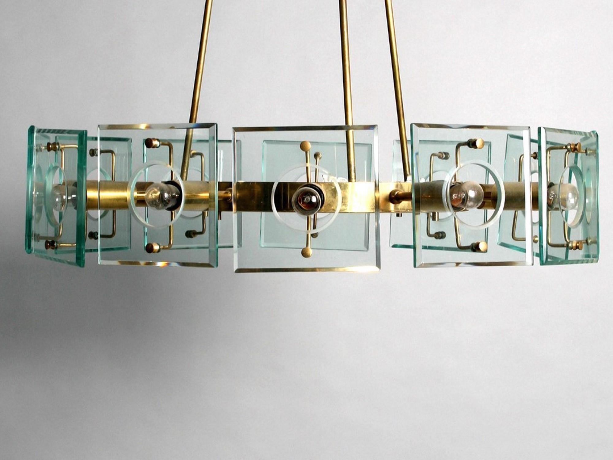 Elegante lampadario di grandi dimensioni in ottone e vetro con dodici bracci in ottone che terminano con paralumi quadrati in vetro con foro centrale. La struttura rotonda in ottone contiene tre steli in ottone che terminano con un fissaggio a