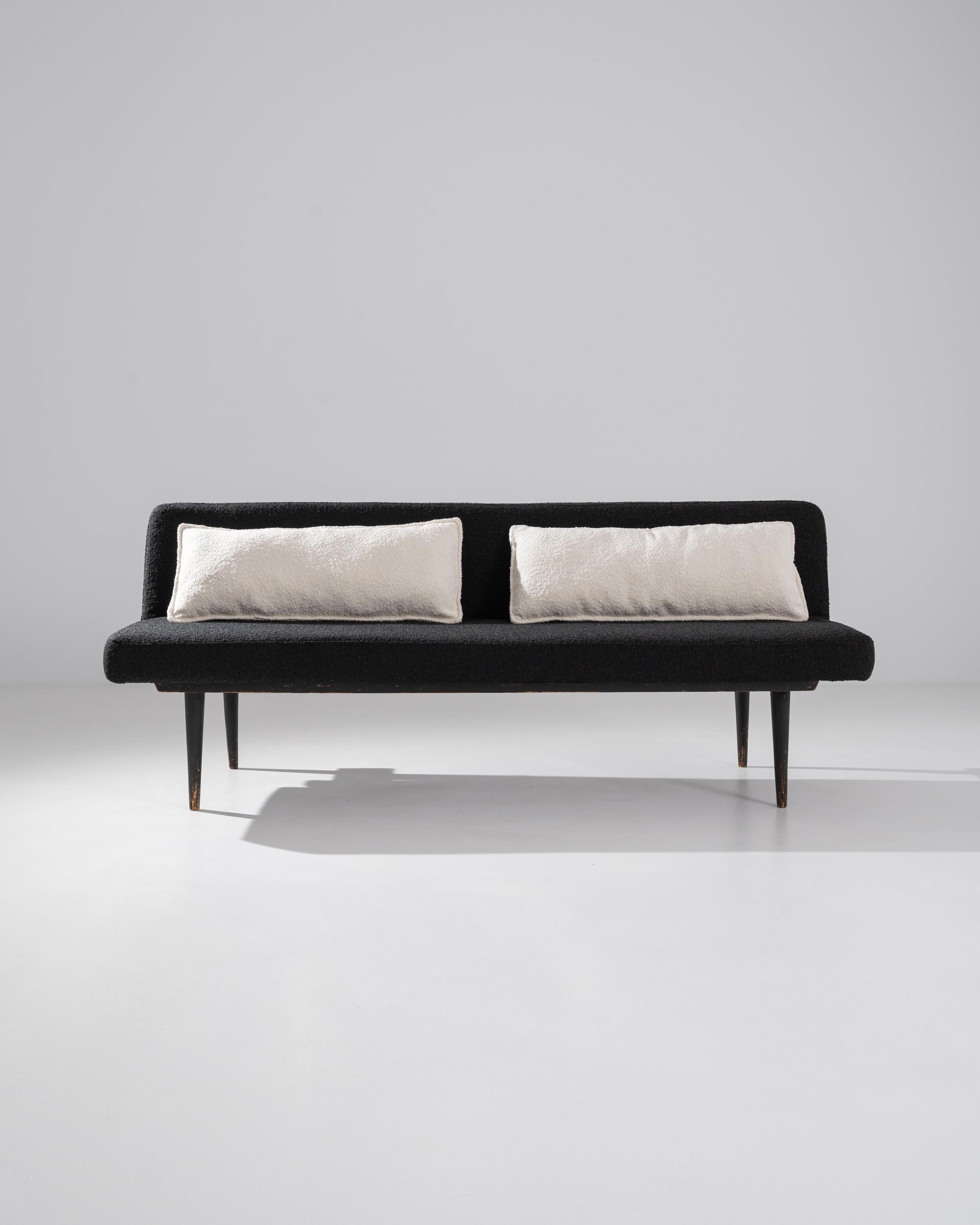 Both practical and impeccably stylish, this vintage sofa bed is a minimalist gem. Made in Central Europe in the 20th century, the form is pared back to its essentials for a graphic silhouette. Slender wooden legs taper to a sharp point; the rounded