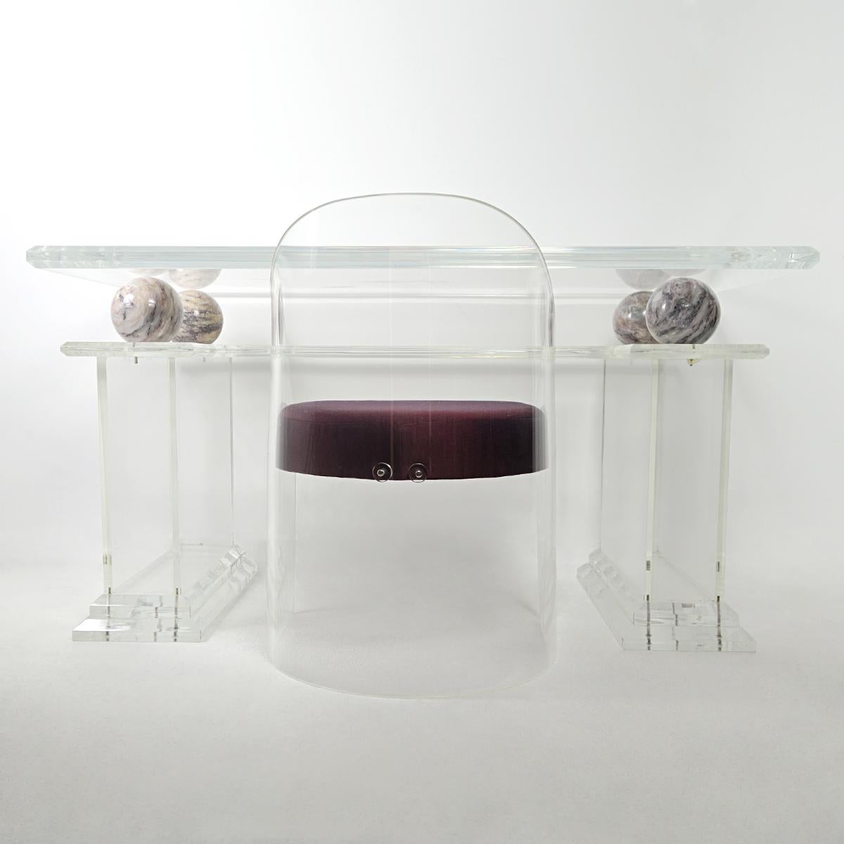 Stunning writing table (or vanity) made of Lucite, in the style of Charles Hollis Jones.

This solid and heavy piece consists of two (hollow) columns, a lower shelf and a slightly larger top resting on four marble balls. The matching chair has
