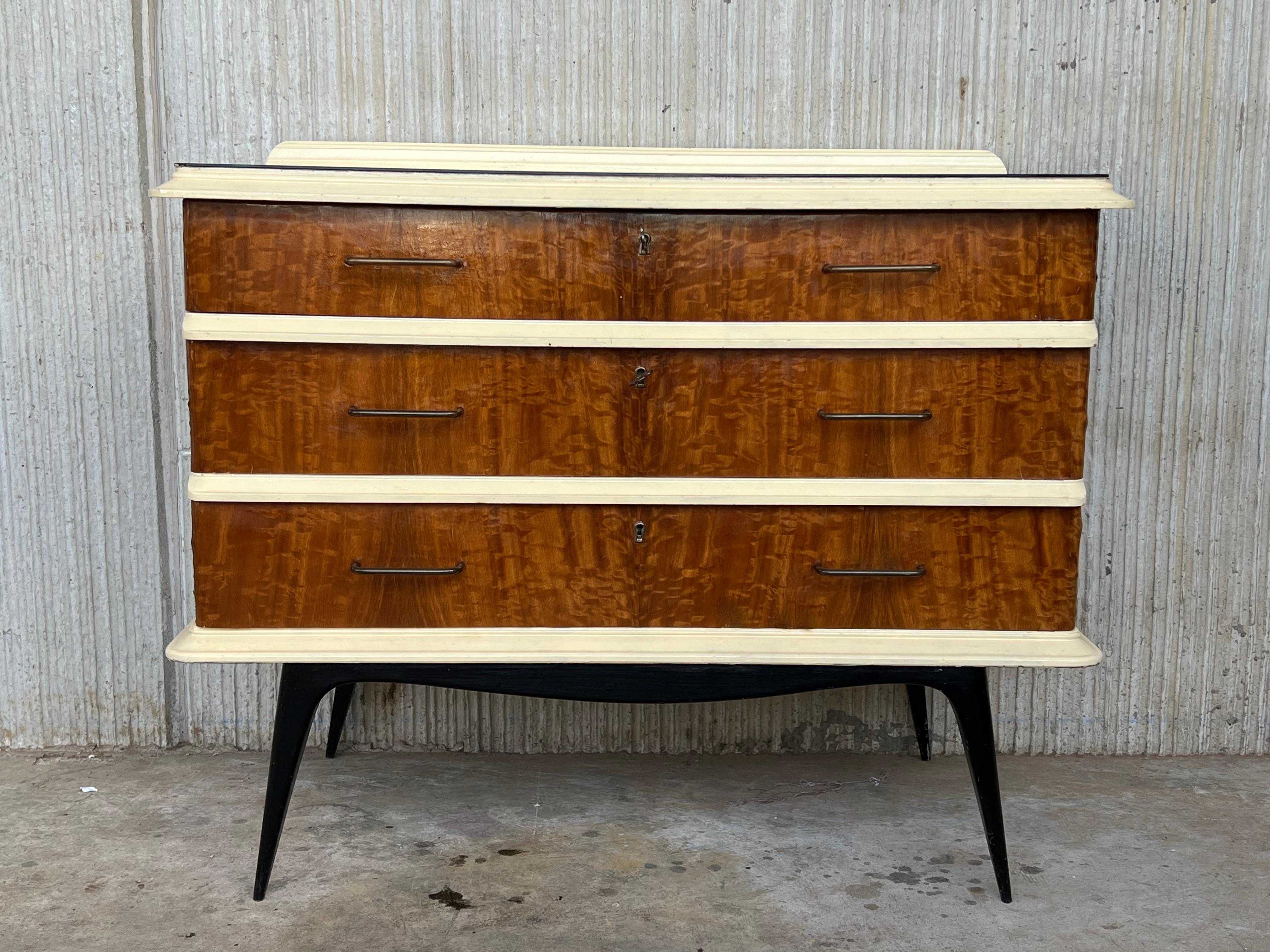 Commode or chest of drawers with three drawers and crest . Are made of wood and veneer and finished with cream lacquered wood in edges and black ebonized legs .
The drawers have a workable lock

We have matching nightstands.