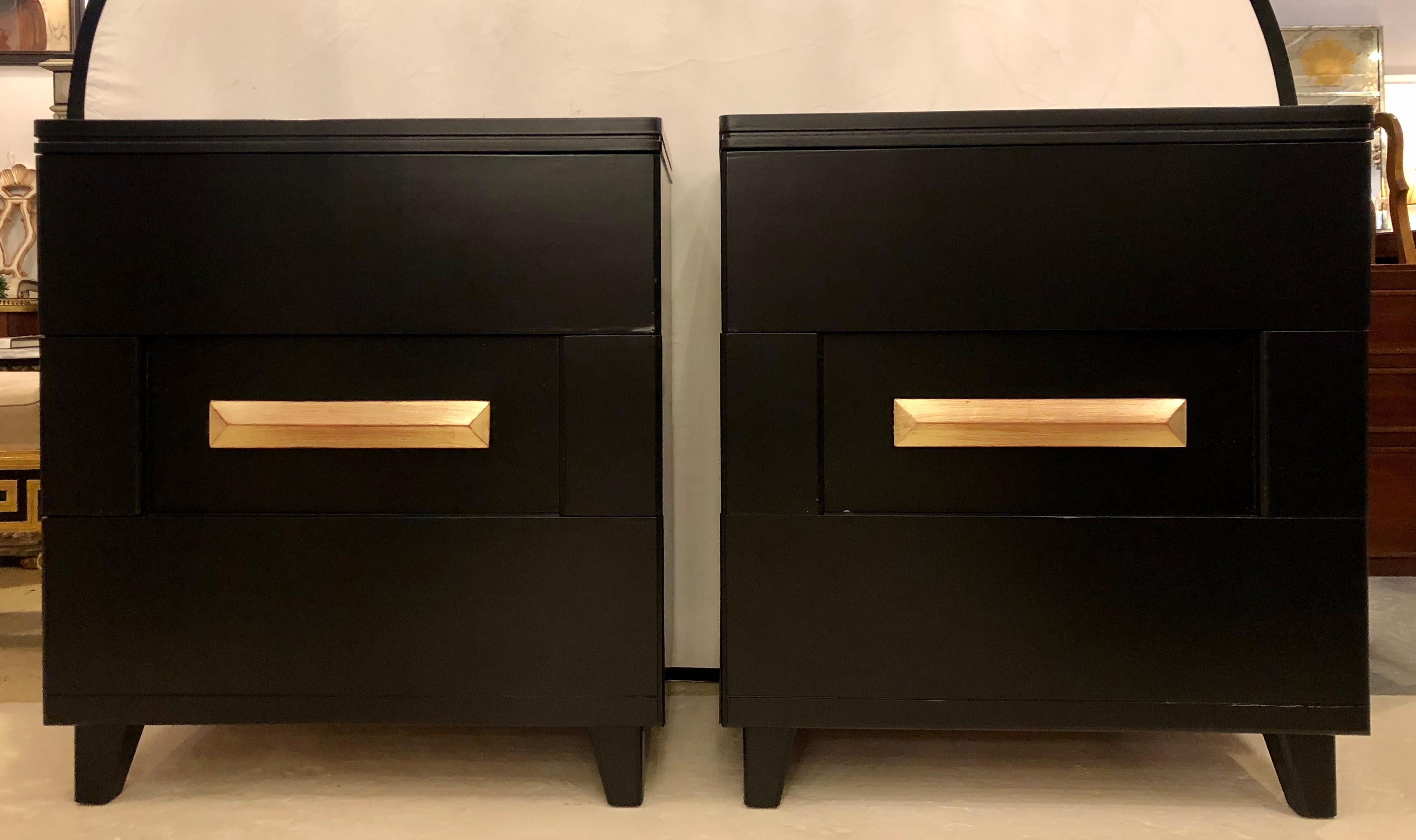 Mid-Century Modern chests or nightstands. A pair of ebony Hollywood Regency. An impressive pair of ebony chest, dressers or nightstands with three drawers in a box form with gilt gold center drawer pulls. All drawers open effortlessly.