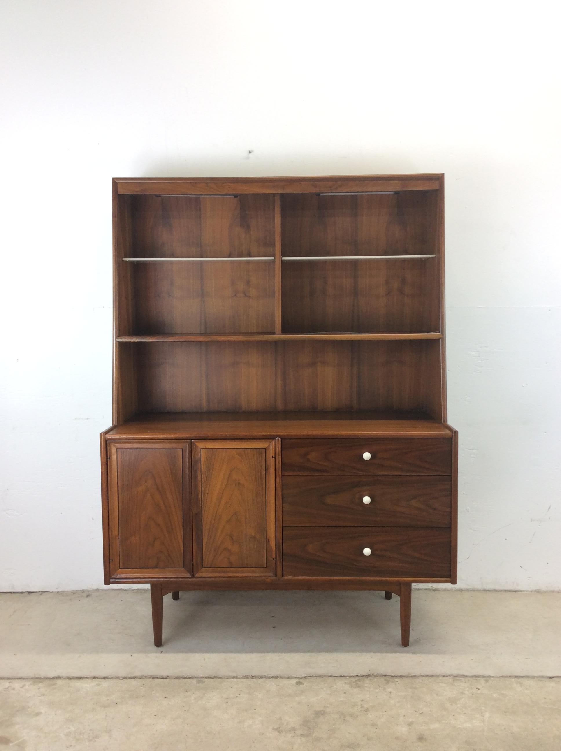 This mid century modern china cabinet from the Declaration line by Drexel features hardwood construction, beautiful walnut veneer with original finish, two adjustable milk glass shelves up top, cabinet with interior shelf below, three dovetailed
