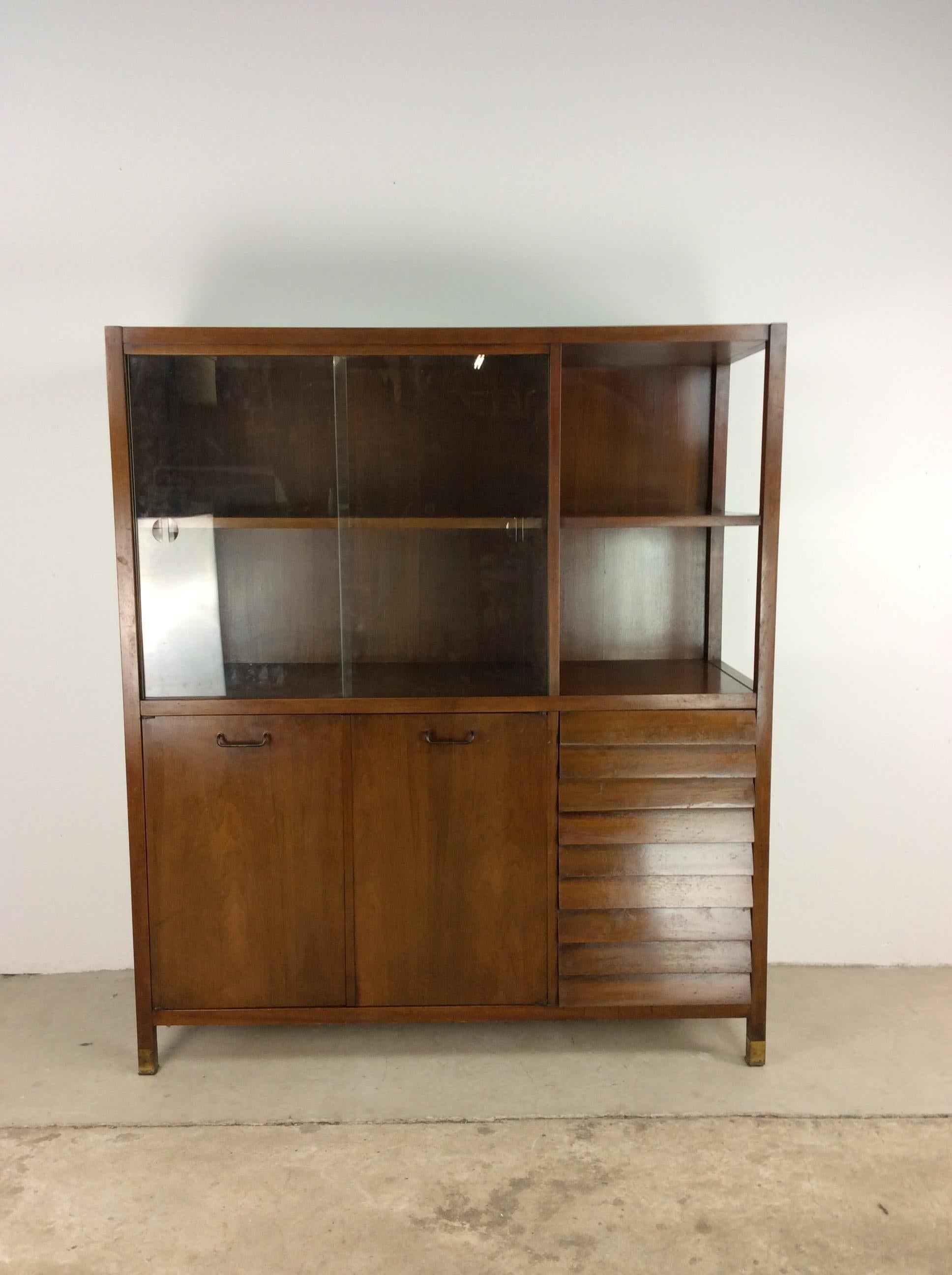 This Mid-Century Modern china cabinet / server from the Dania line by American of Martinsville features hardwood construction, walnut veneer with original finish, three dovetailed drawers with louvered fronts, static shelving behind sliding glass