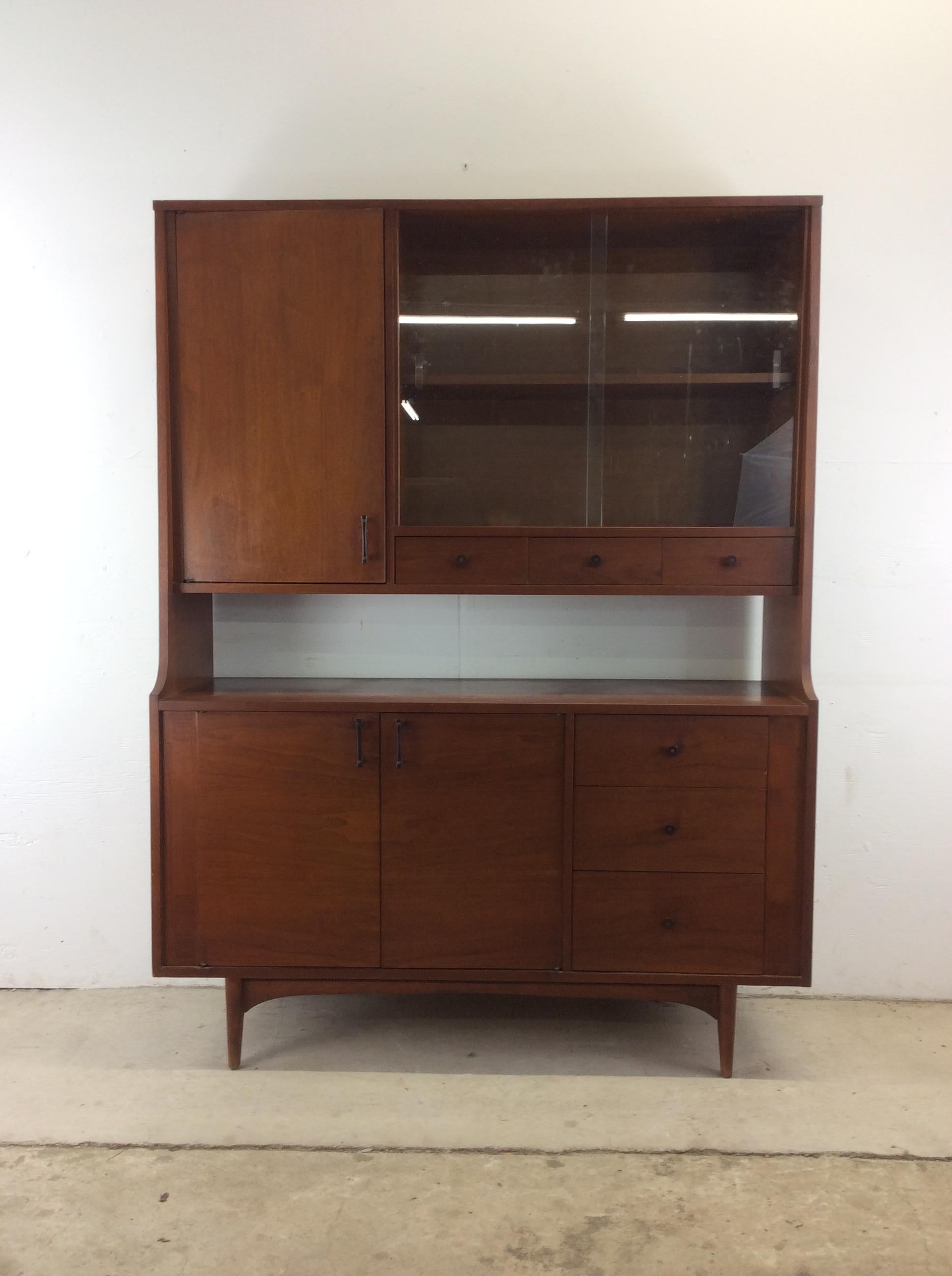 This mid century modern china cabinet by Kroehler features hardwood construction, one piece design, walnut veneer with original finish, five dovetailed drawers with brass accented hardware, two cabinets with adjustable shelves, and sliding glass