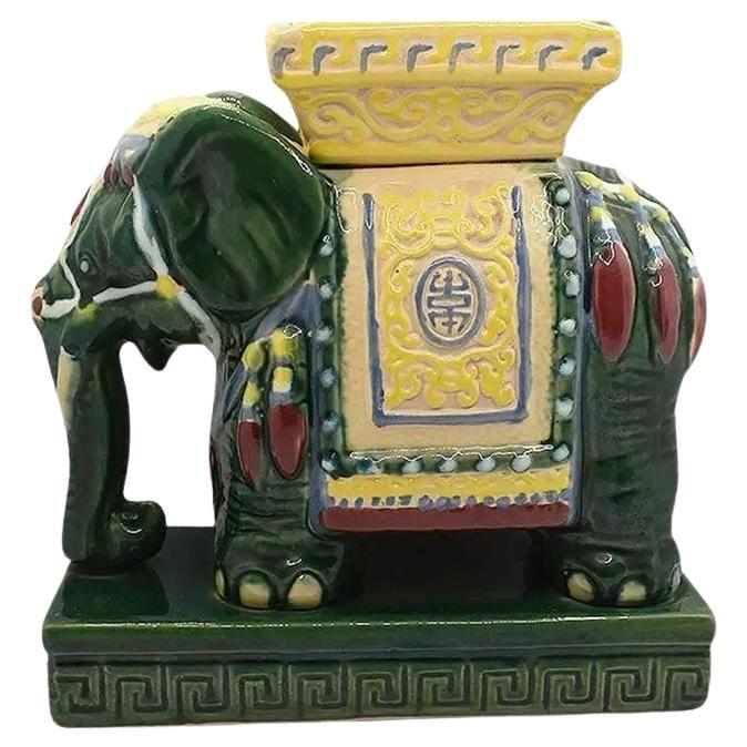 A green and yellow ceramic elephant ashtray or catchall. Reminiscent of the ever-popular chinoiserie elephant garden stool, this tall ashtray features an elephant body, with a square ashtray at the top. The elephant has his trunk down and is