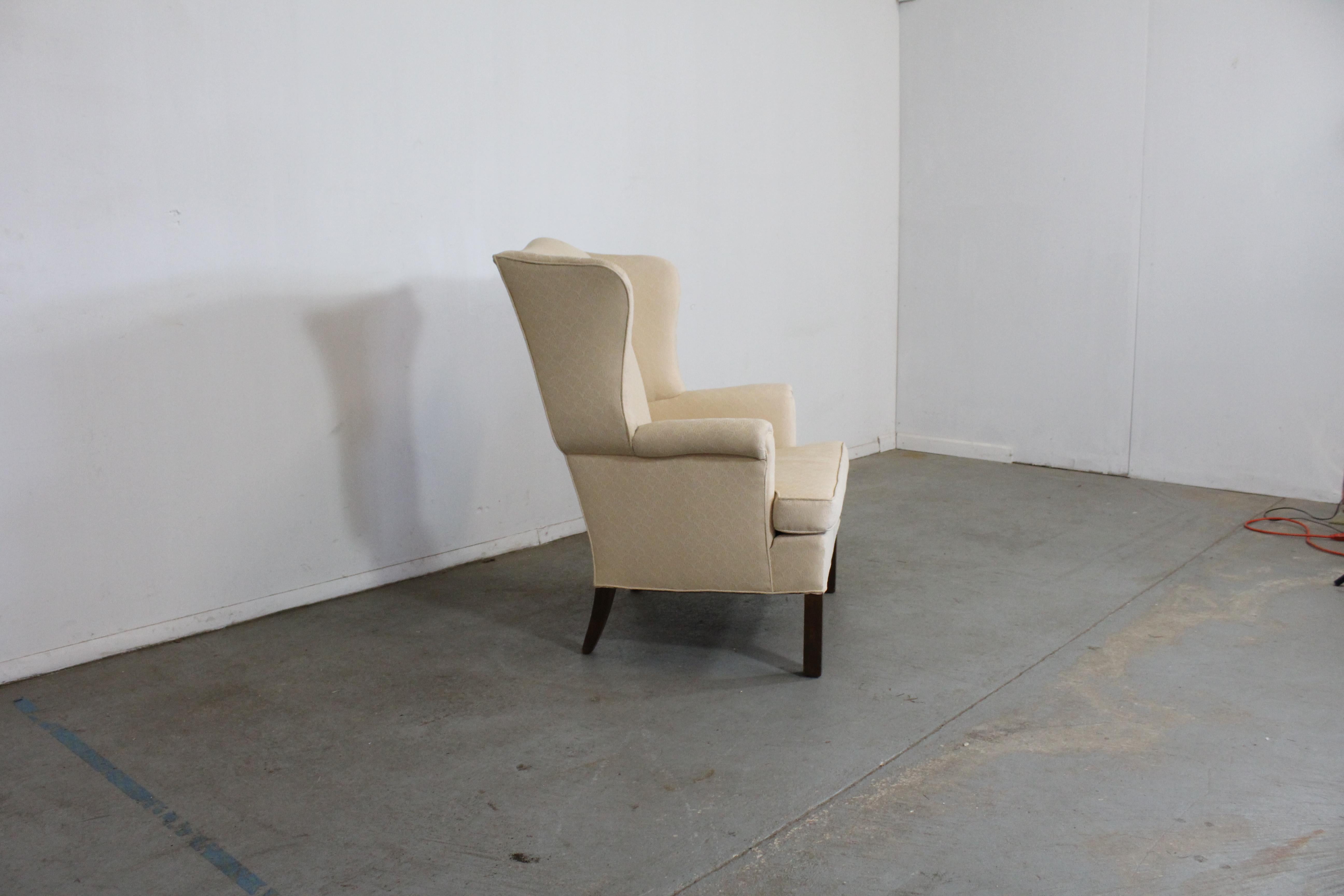 Offered is a vintage wing back chair with textured white upholstery and wood legs. It is in good condition with usable upholstery, showing some staining on the fabric and minor scratches on the legs. It is structurally sound. A great, sturdy chair