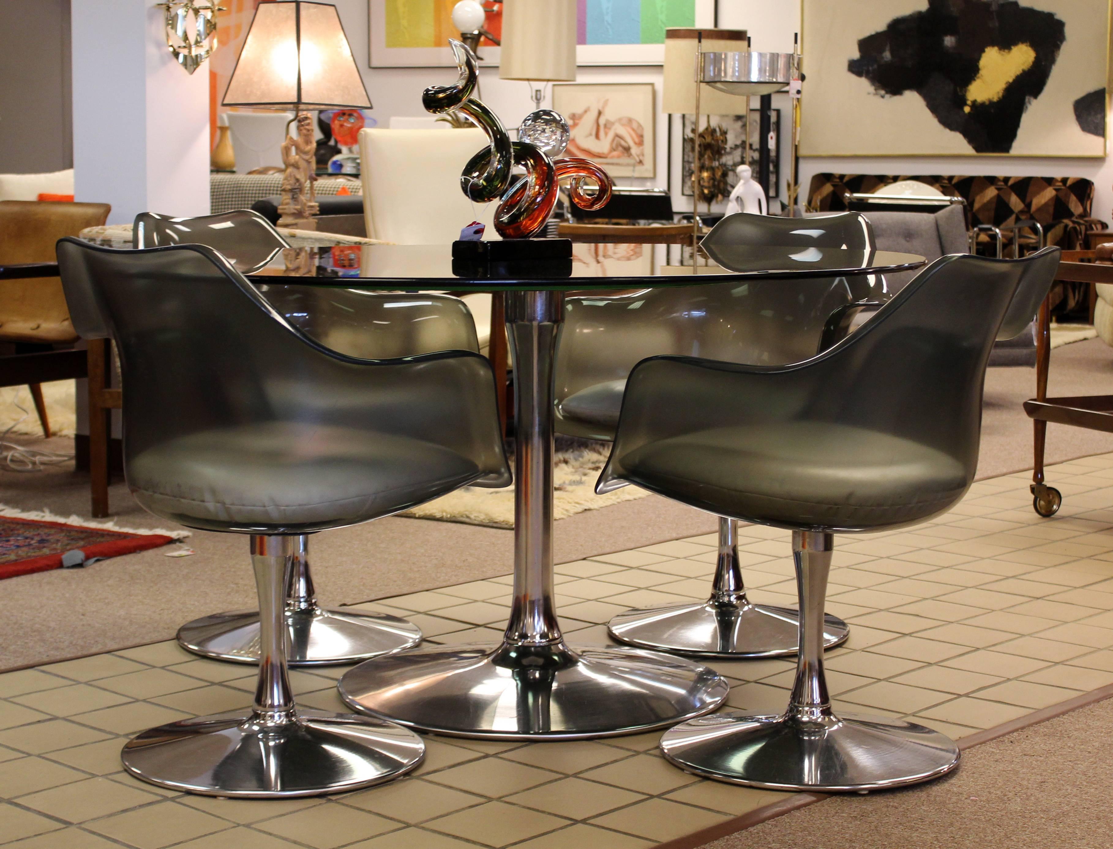 Nous vous proposons un fabuleux ensemble de salle à manger:: comprenant une table avec un plateau en verre fumé et quatre fauteuils en coquille avec des sièges en Lucite fumé:: par Chromcraft:: vers les années 1970. En très bon état. Le plateau en