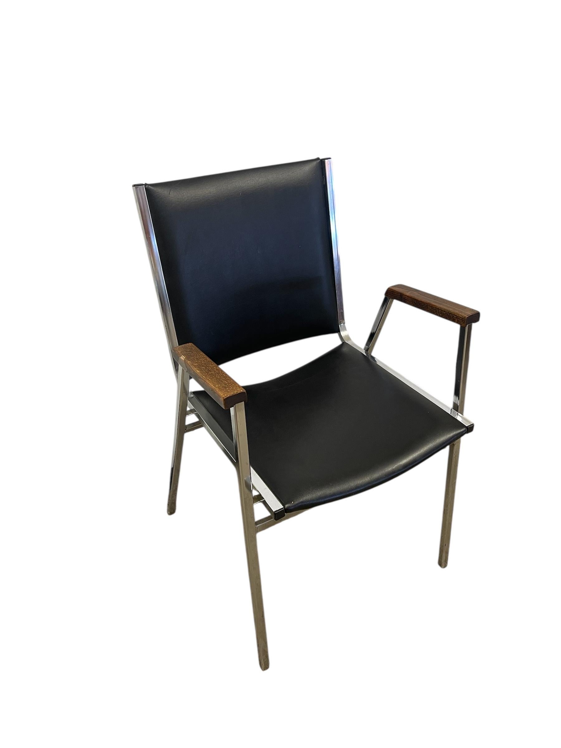 This vintage mid-century modern armchair from the 1970s features a minimalist frame constructed from tubular chrome, paired with black faux leather upholstery on the seat and backrest. The chair's geometric silhouette is accented by gently curved