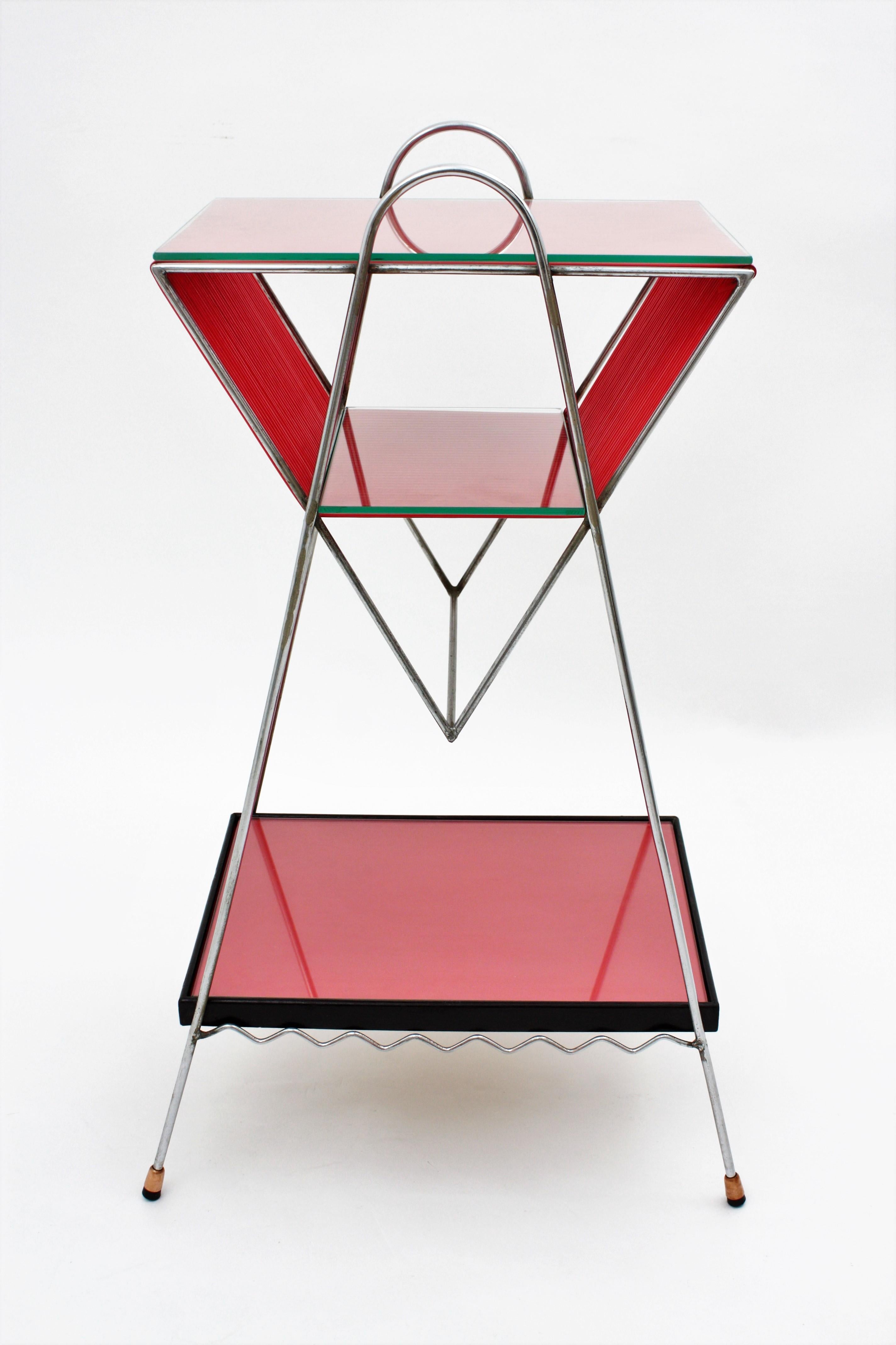 Mid-Century Modern side table or magazine rack with three levels. The structure is made of chromed iron. The lower tray is made of lacquered red and black wood, and the upper trays are made of red scoubidou or plastic thread. Its geometric design