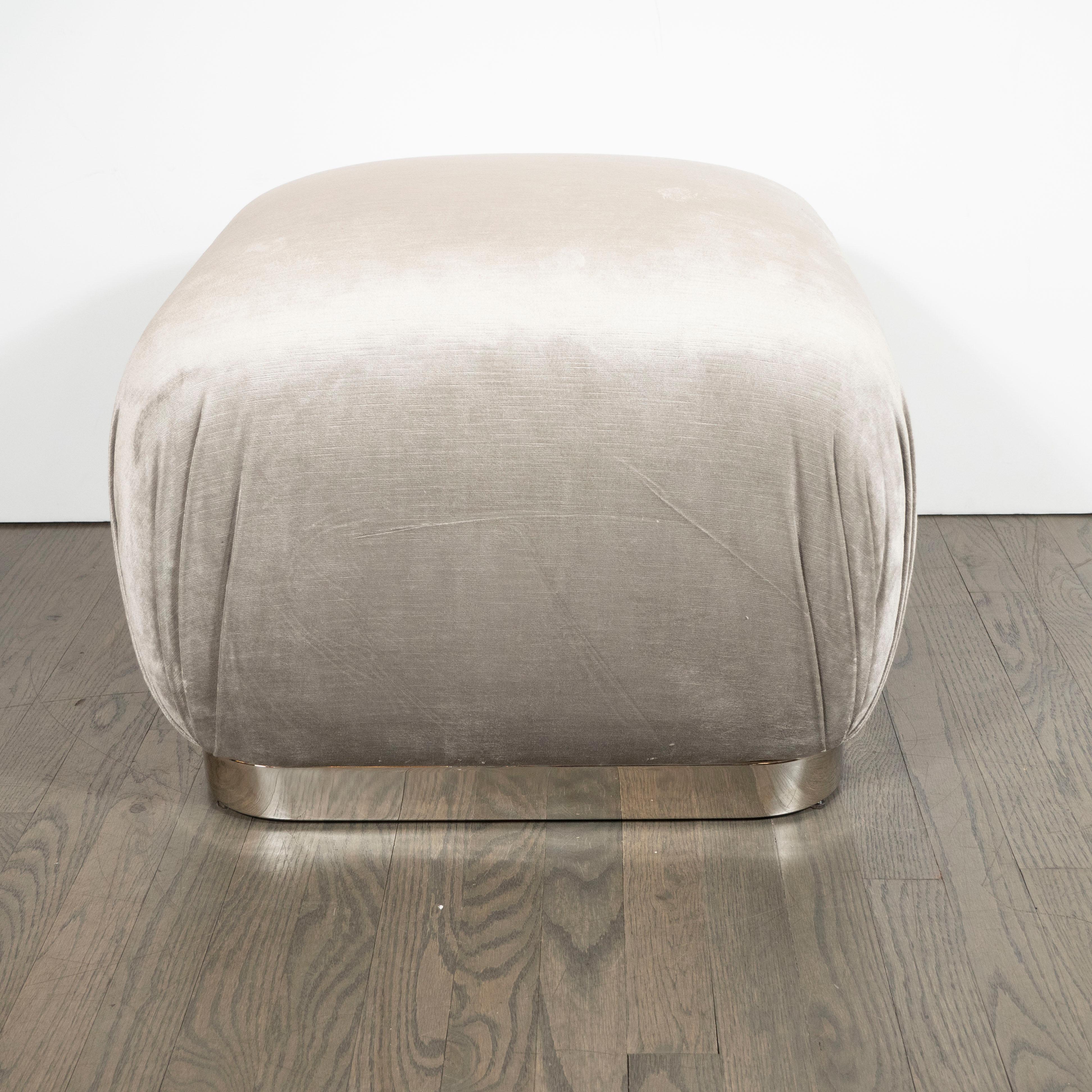 This sophisticated Mid-Century Modernist soufflé pouf, realized in the manner of Karl Springer, feature a lustrous square chrome bases with rounded edges and platinum velvet upholstery. With its austere lines and luxe materials, this piece manage to