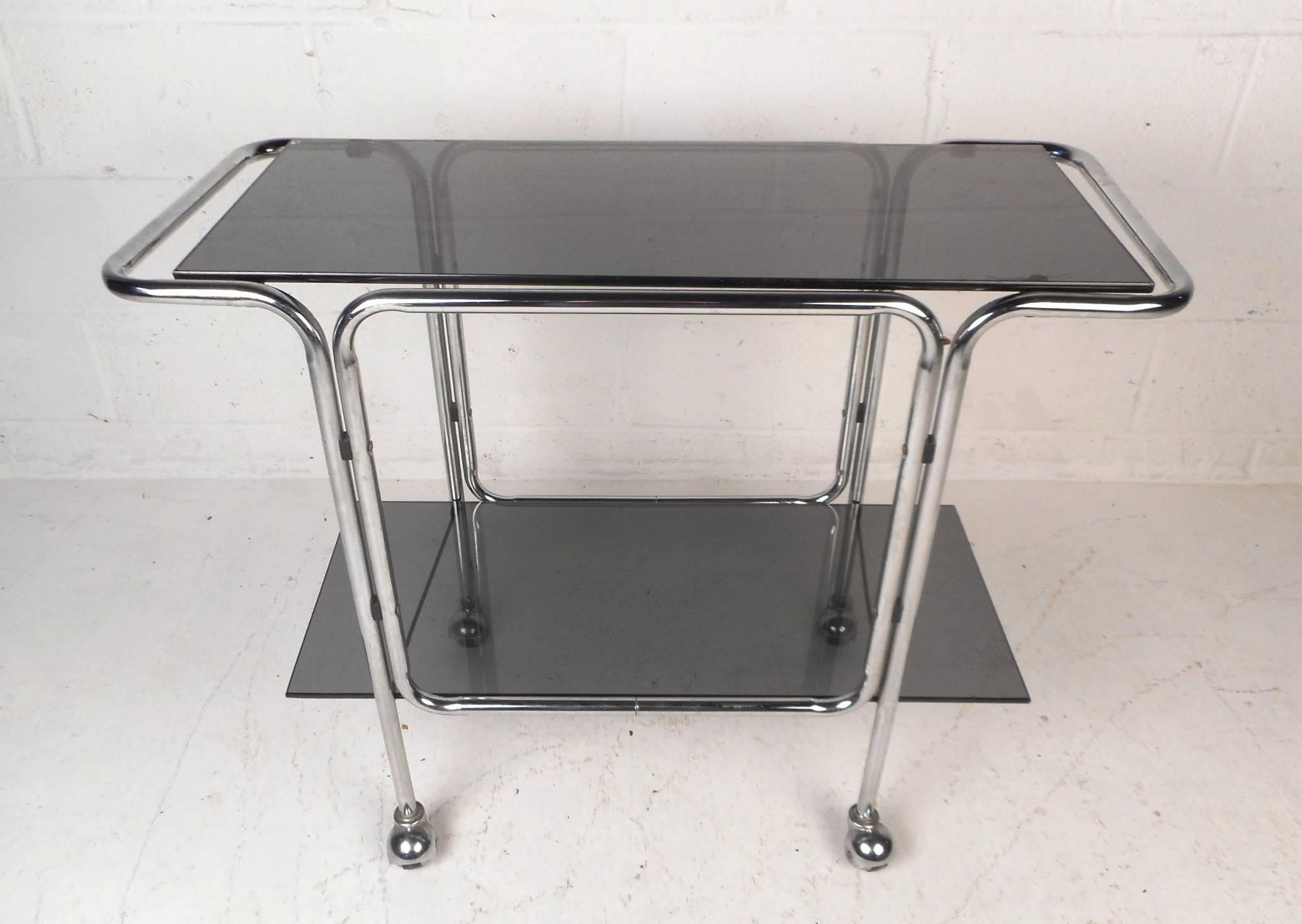 A stunning vintage modern serving cart with two smoked glass shelves and castors for convenience. The sleek chrome tubular frame and two tiers for setting items on shows quality design. Works perfectly as a functioning serving cart or simply a