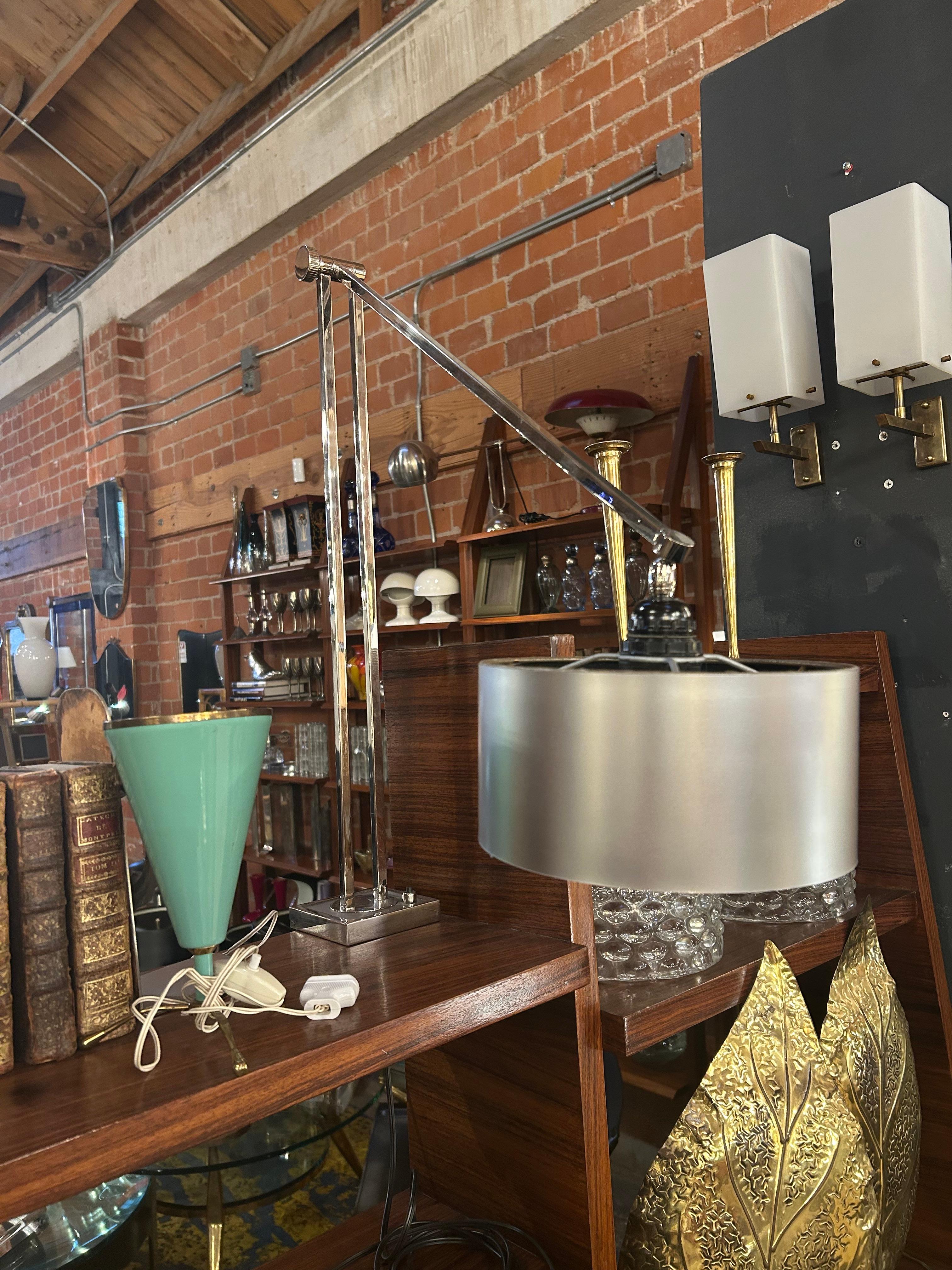 Un'elegante lampada da scrivania a morsetto, moderna e di metà secolo, con una struttura in cromo lucido e un braccio oscillante regolabile. La lampada è progettata con una pratica base a morsetto che le permette di essere montata in modo sicuro su